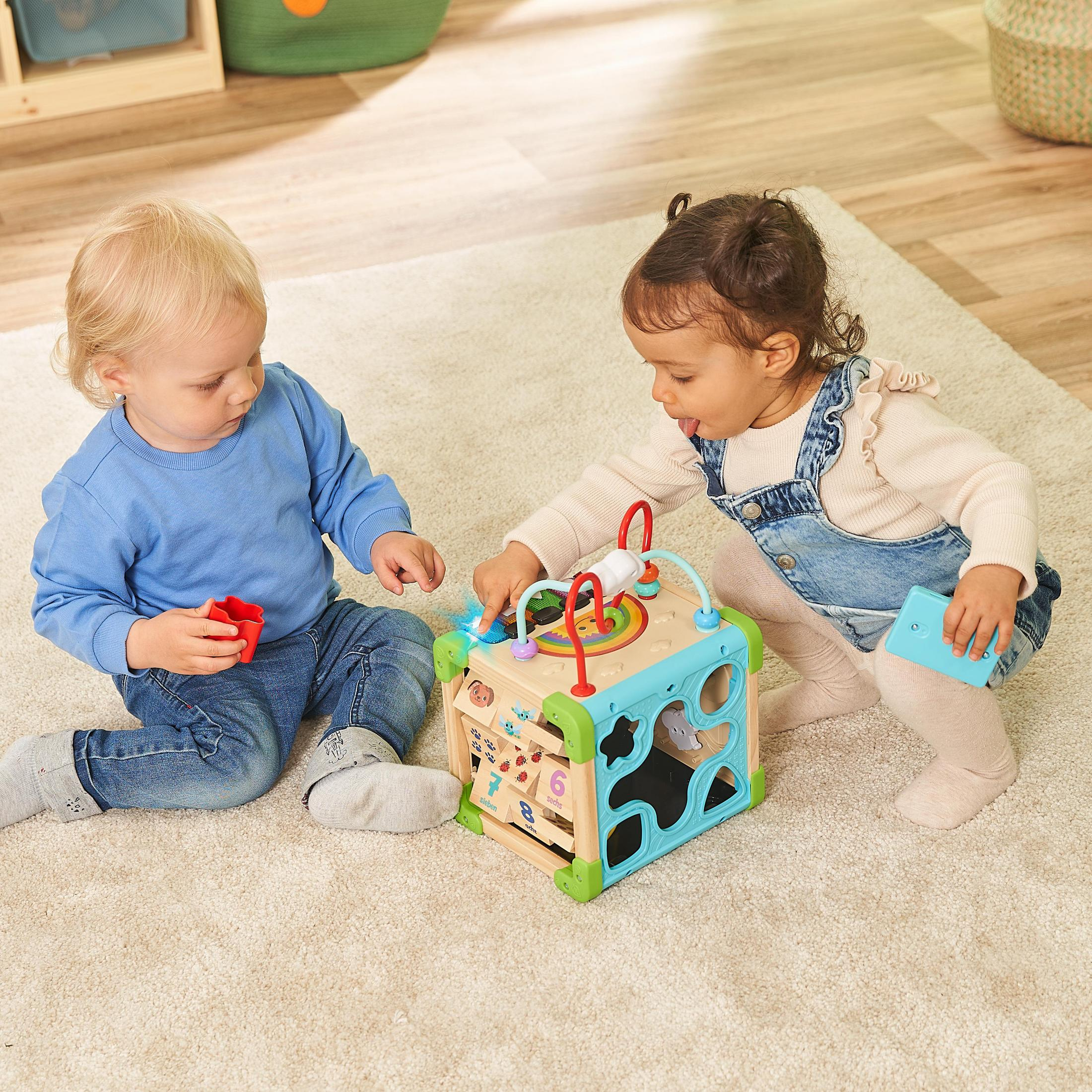 Zwei Babys spielen mit einem Spielzeugwürfel.