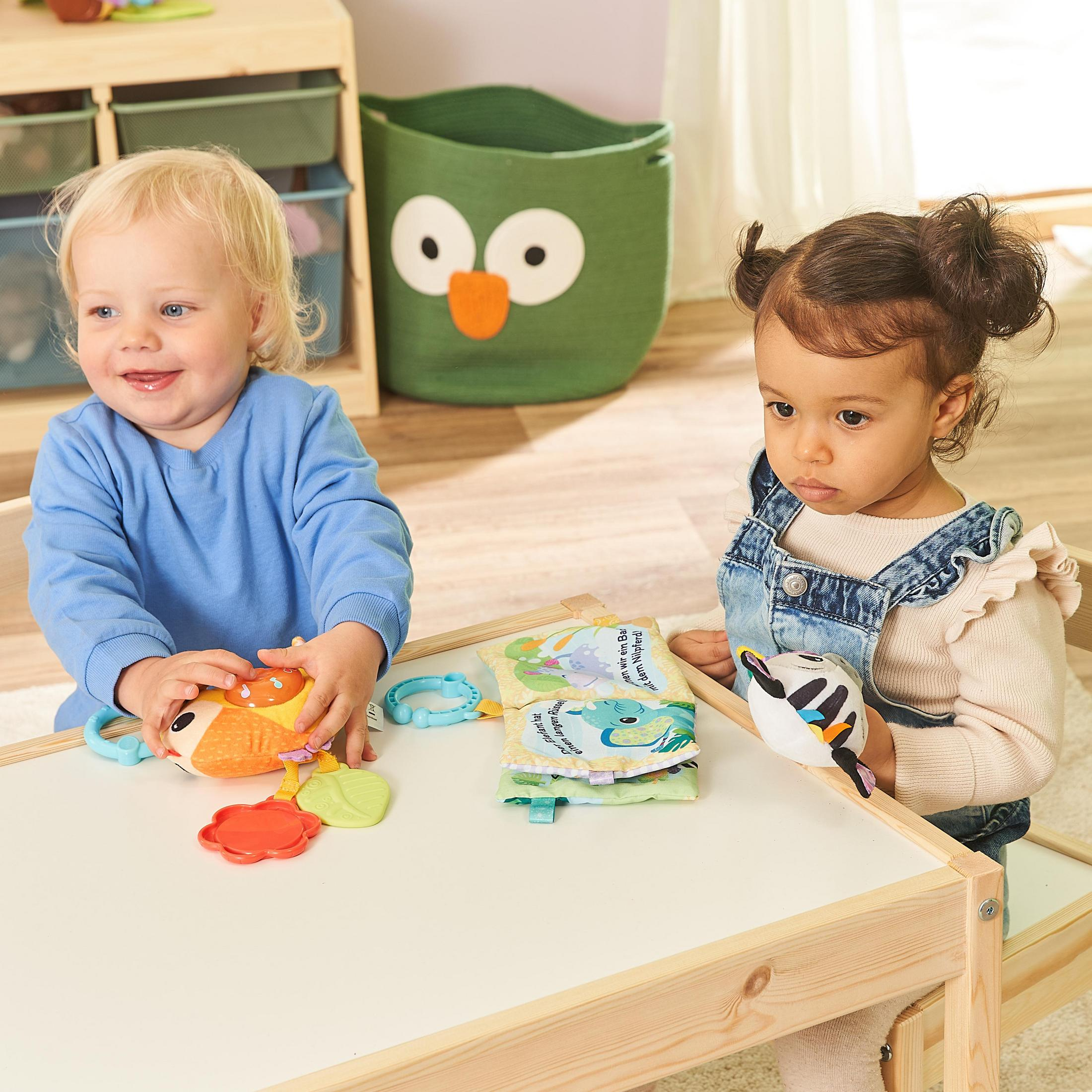 Zwei Babys spielen mit Spielzeug an einem Tisch.