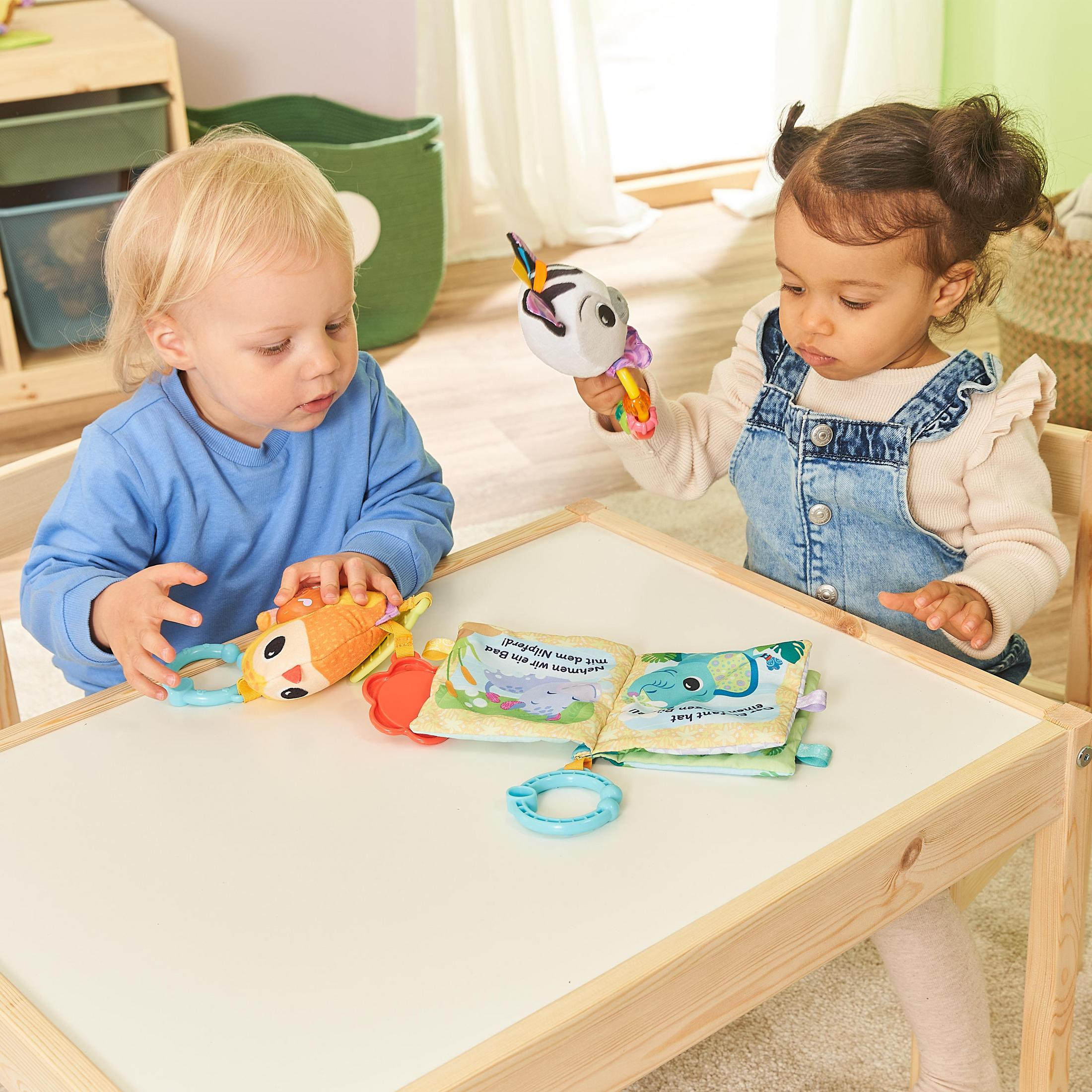 Zwei Kleinkinder spielen mit Kuscheltieren auf einem weißen Tisch. Eines hält ein Zebra, das andere ein fischförmiges Spielzeug.