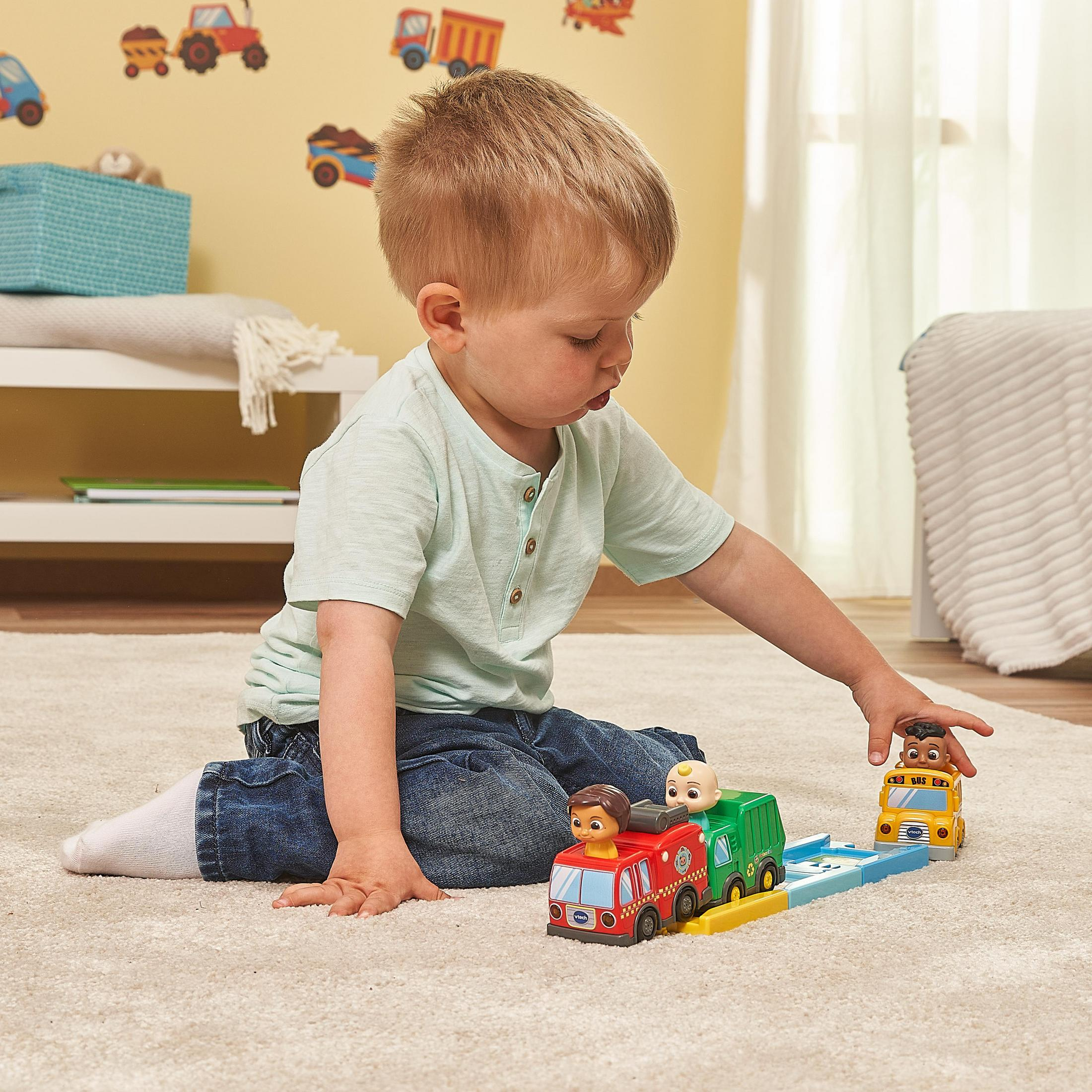 Ein kleiner Junge spielt mit Spielzeug-LKWs auf einem Teppich in einem Zimmer.