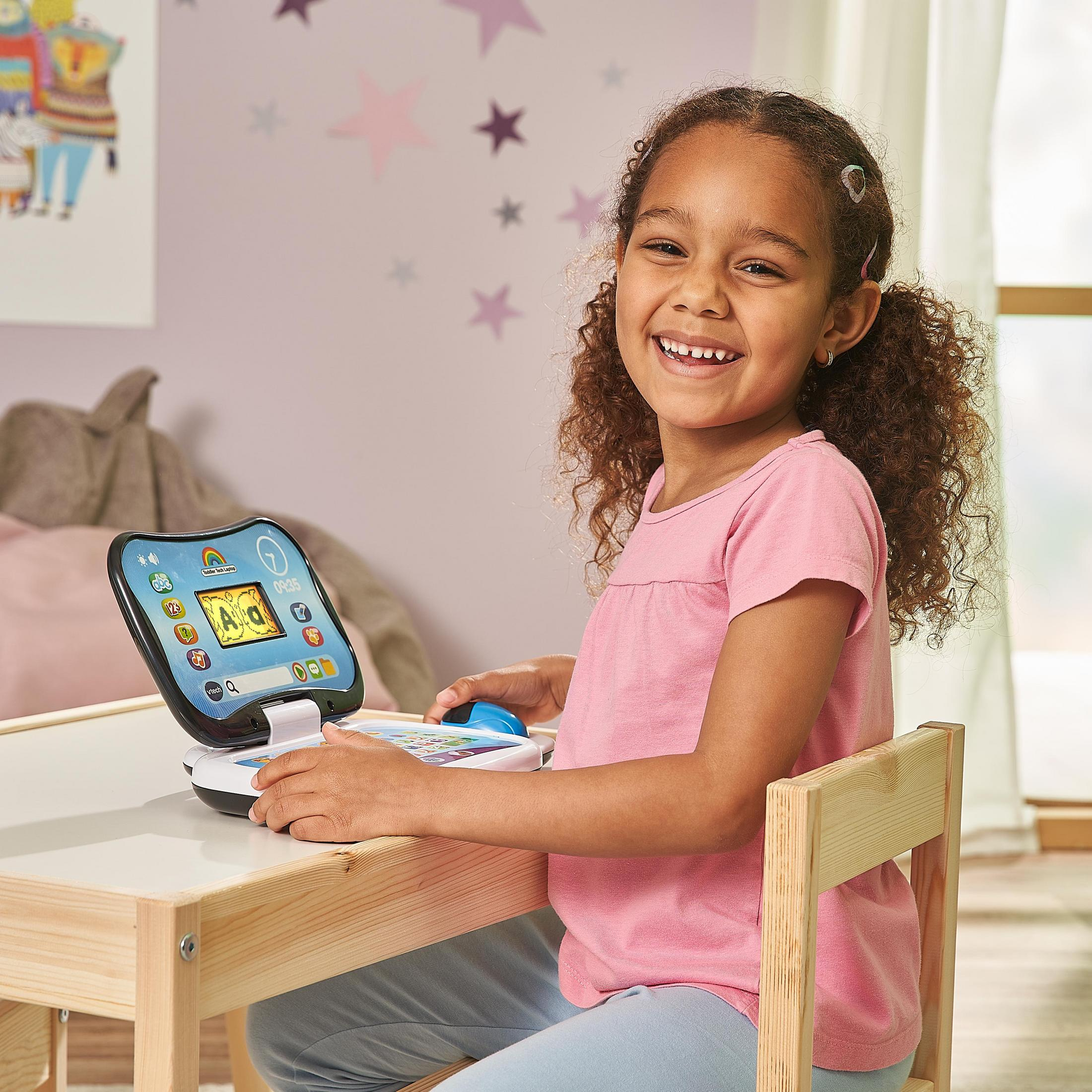 Una bambina usa un laptop giocattolo. Sorride. Lo sfondo è un muro con stelle.