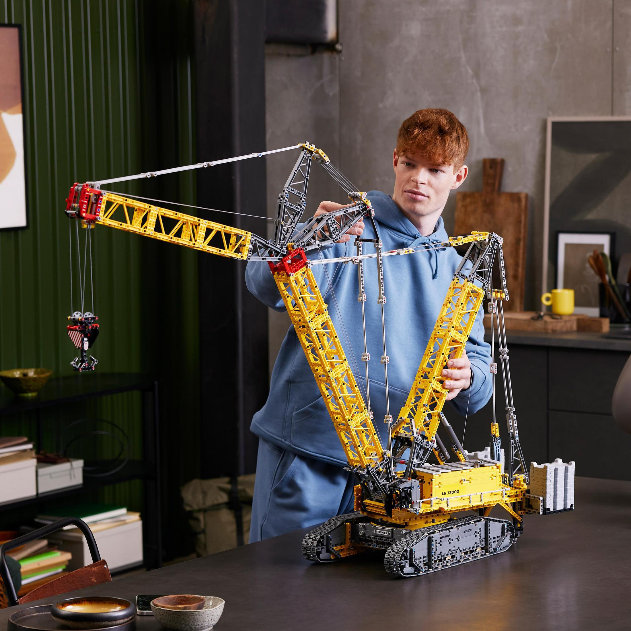 Mężczyzna składający duży, żółto-czarny model dźwigu. Tło: kuchnia.