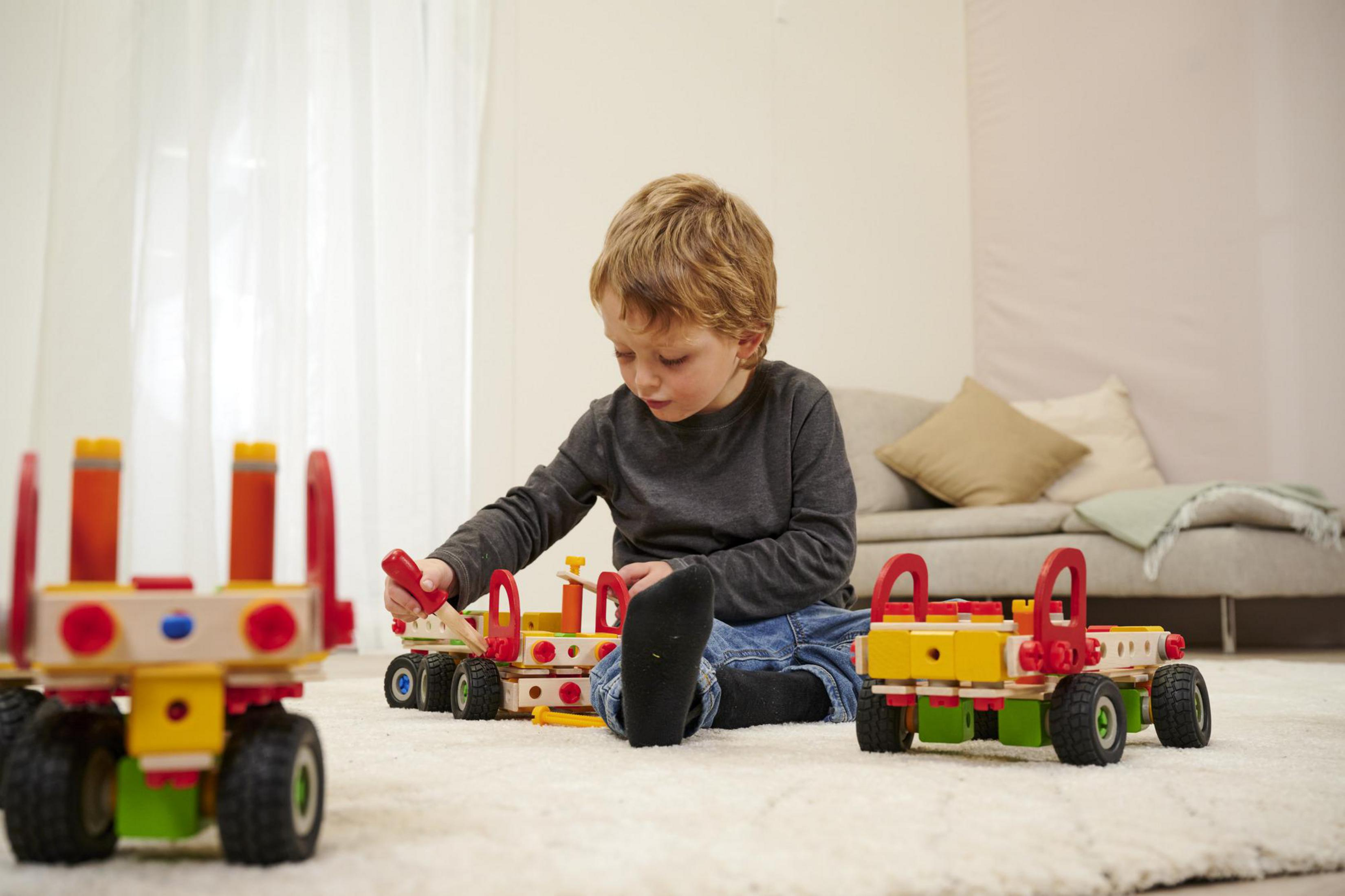 Junge spielt mit Spielzeugautos; drei Autos im Vordergrund.