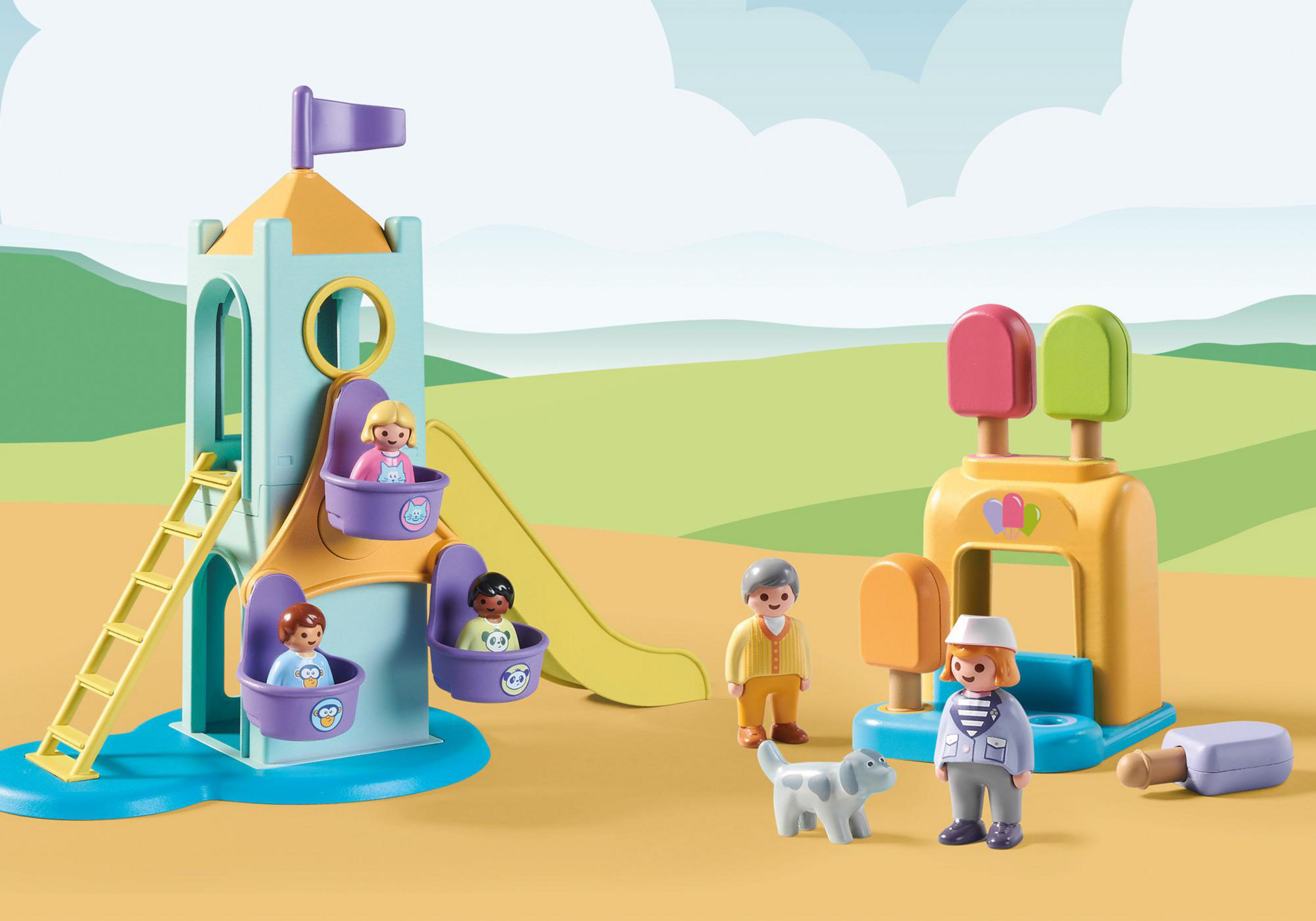 Parco giochi Playmobil con scivolo, torre e personaggi. Erba verde e cielo blu sullo sfondo.