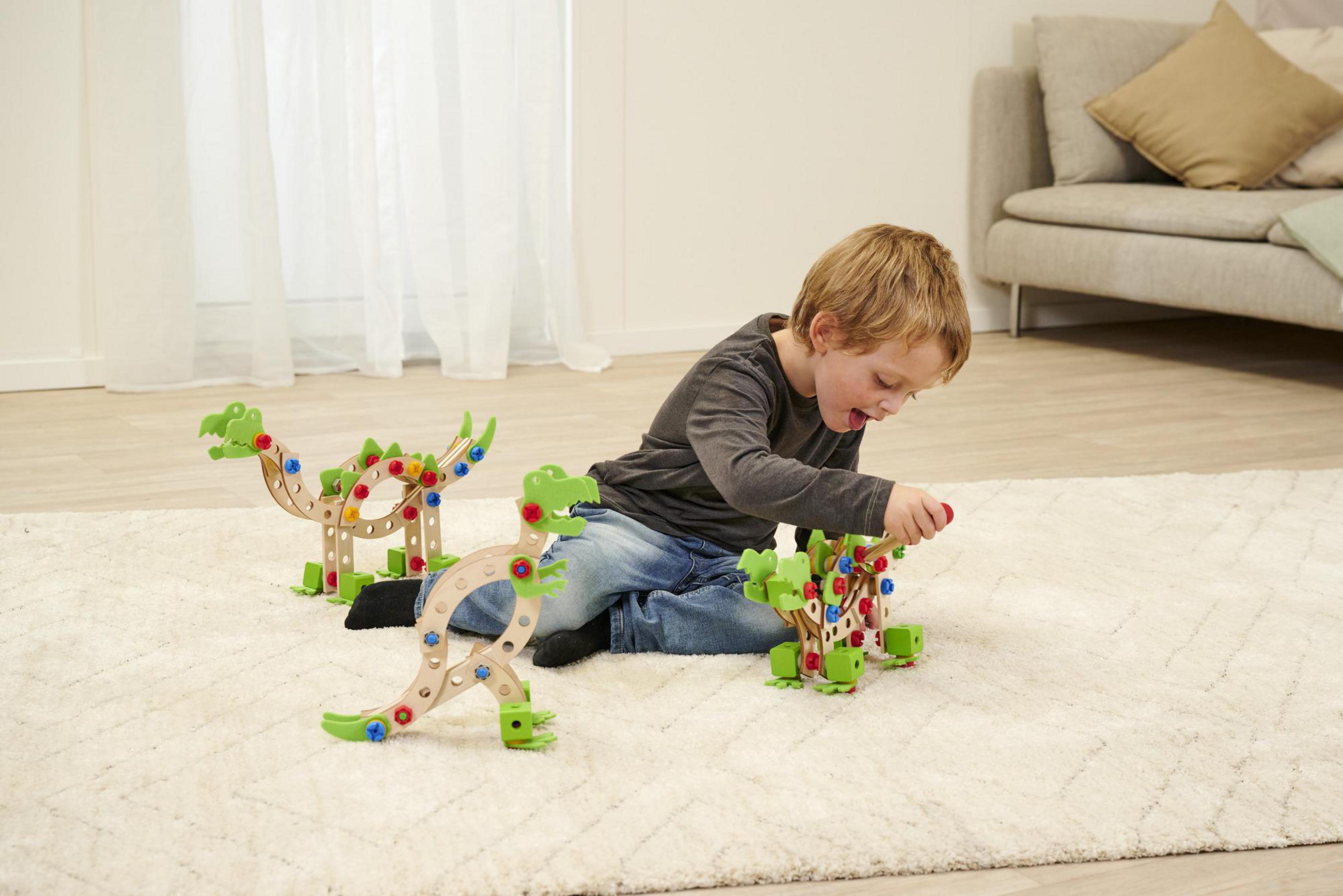 Ein Kind spielt mit Holz-Dinosaurier-Bauspielzeug auf einem Teppich im Wohnzimmer.