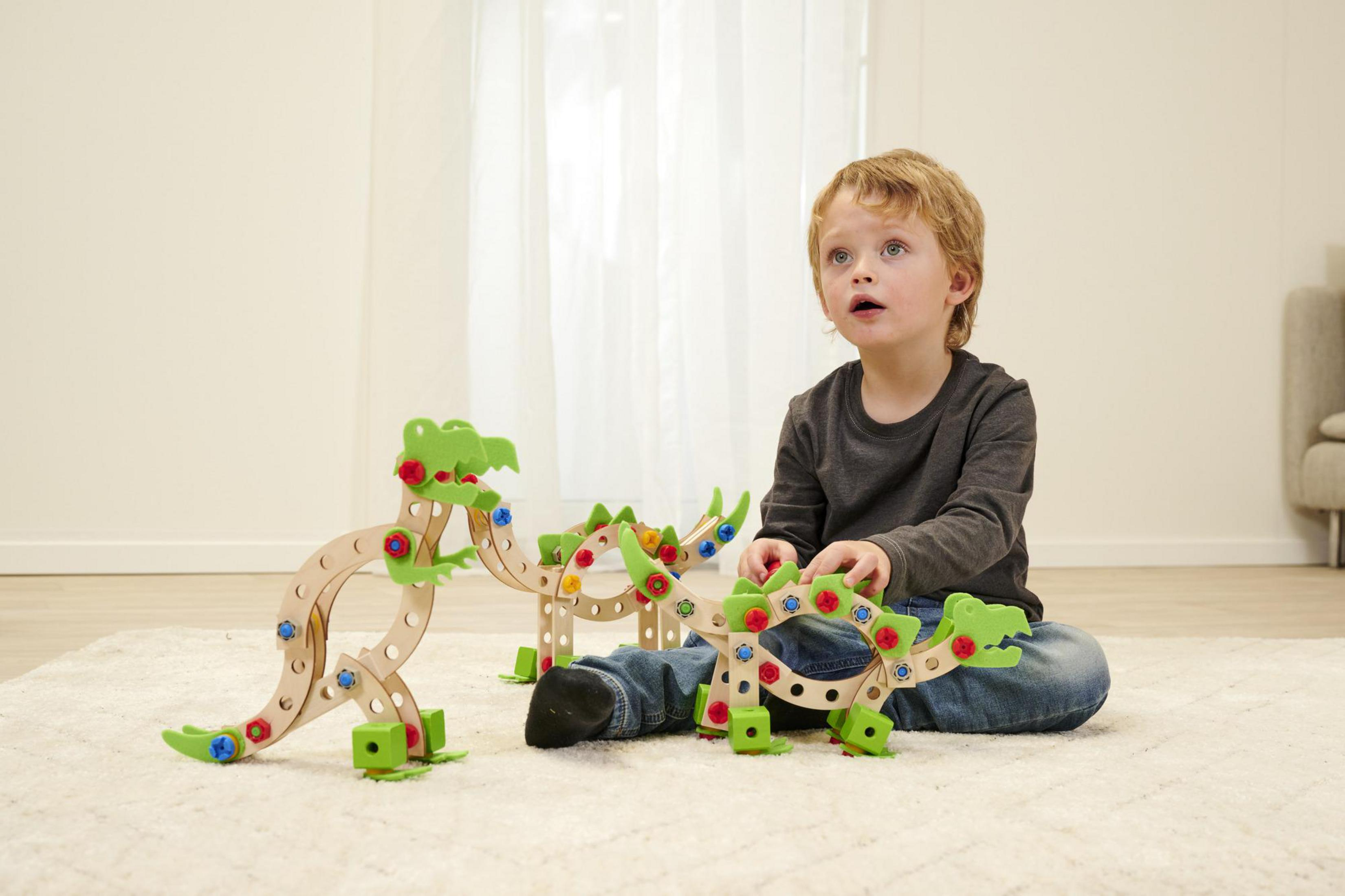 Ein Junge spielt drinnen auf einem weißen Teppich mit Holzspielzeug-Dinosauriern.