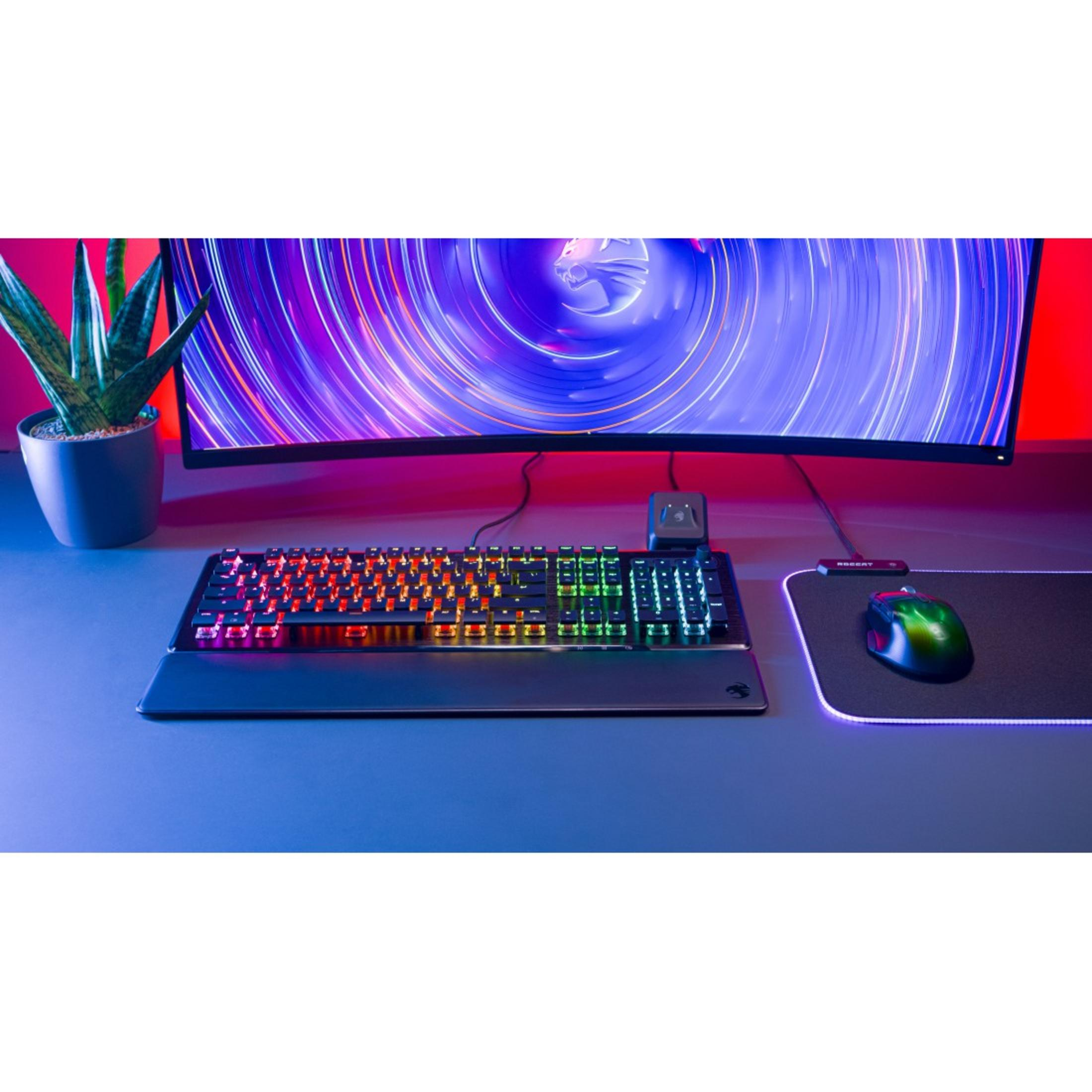Una tastiera e un mouse illuminati su una scrivania. Una pianta e un monitor curvo sullo sfondo.