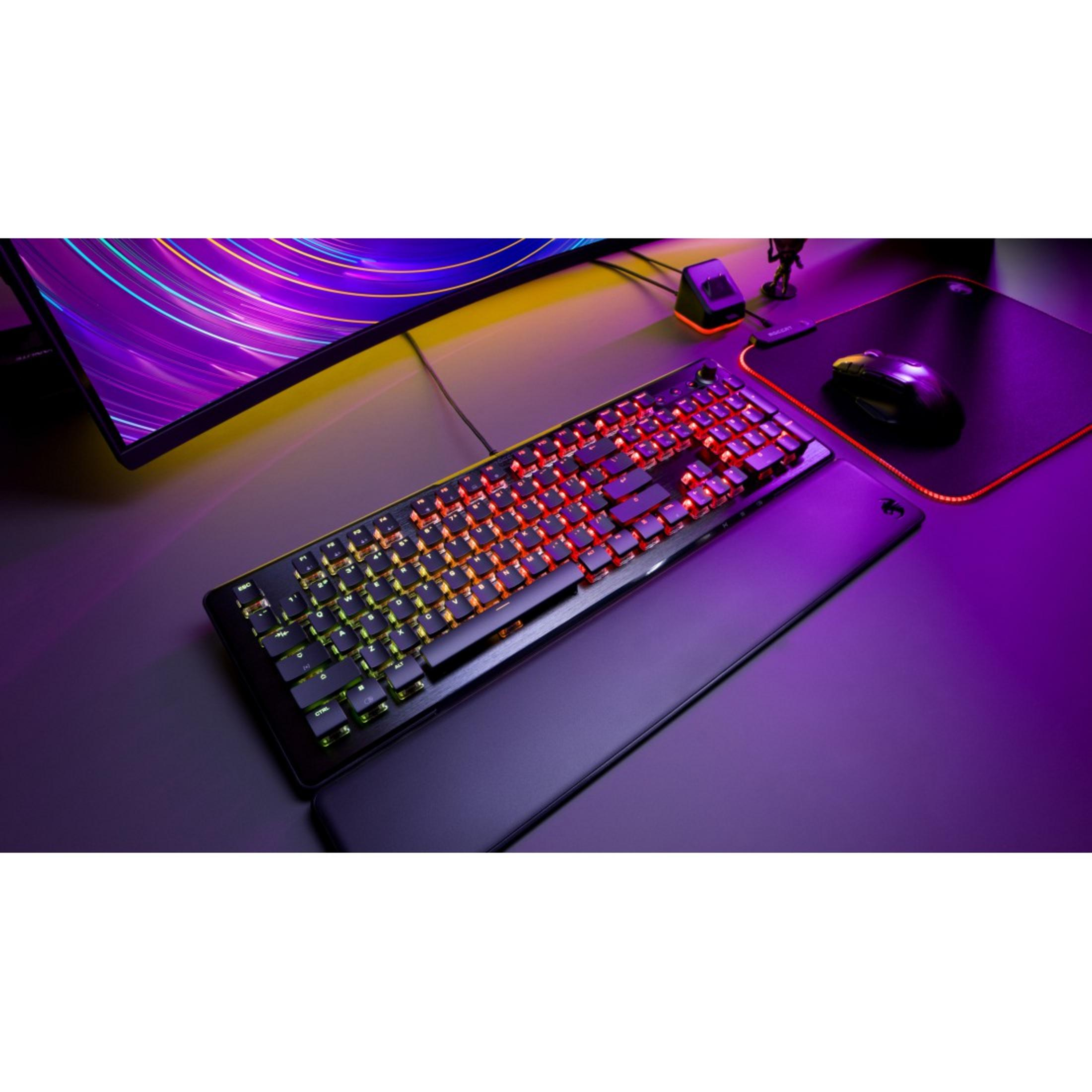 Una tastiera da gioco illuminata con un poggiapolsi nero e un tappetino per mouse è su una scrivania con luci.
