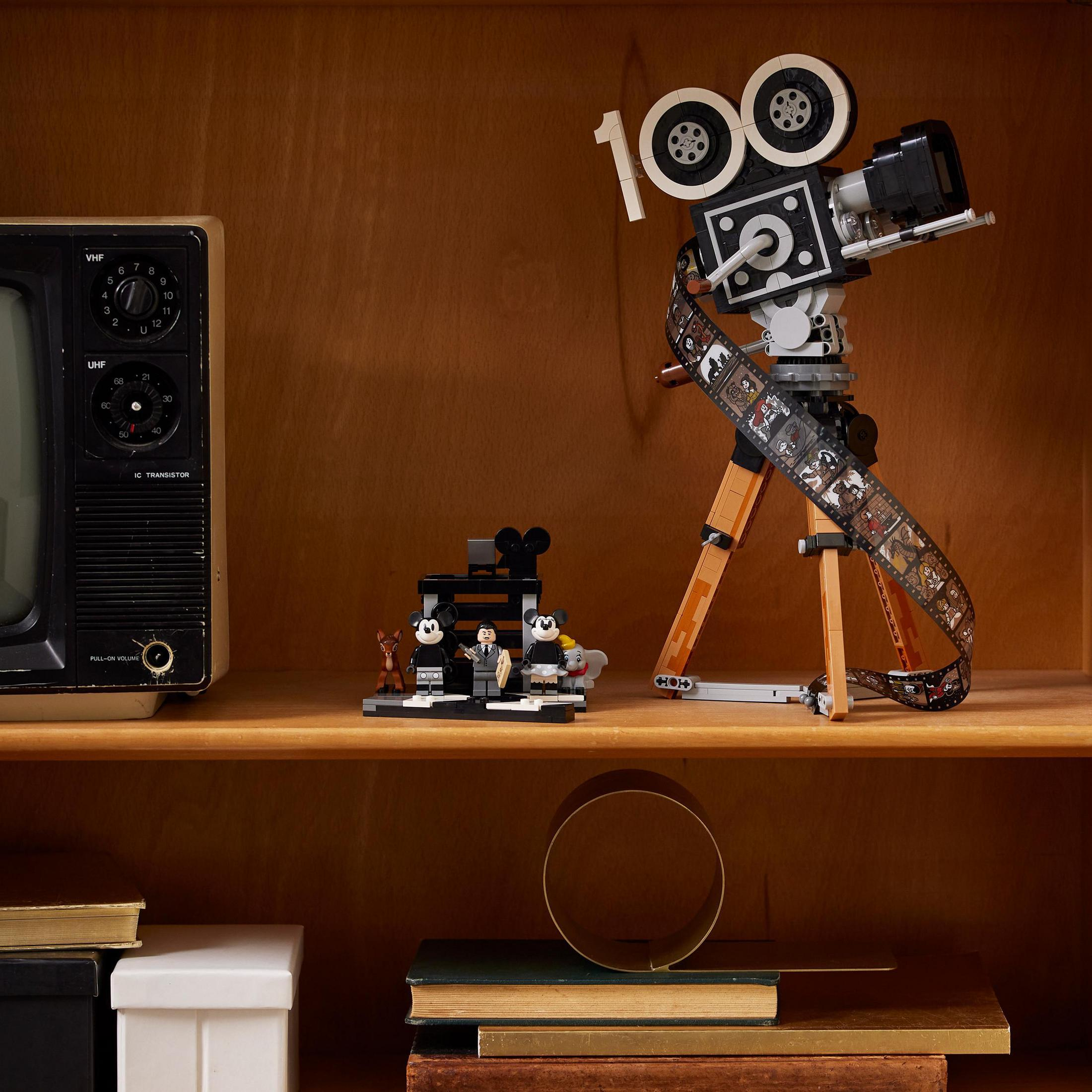 Zestaw filmowy Lego: kamera filmowa ze znakiem 100, taśma filmowa, figurki i telewizor retro na półkach.