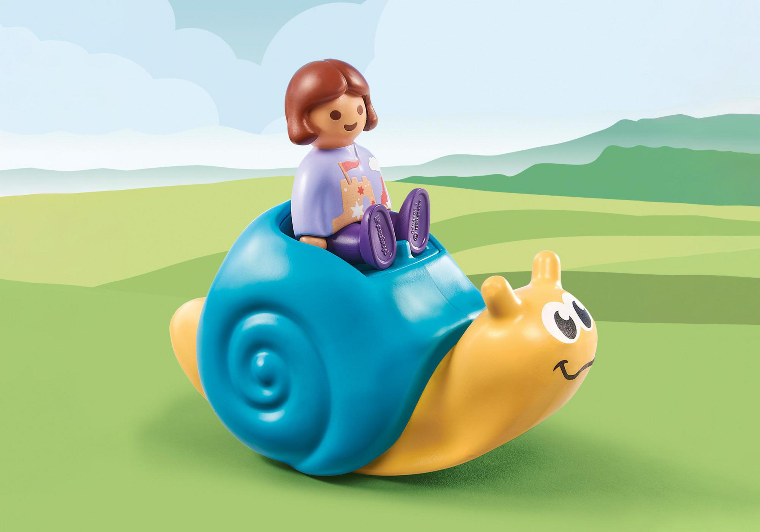 Playmobil-Figur reitet auf gelbem Schneckenspielzeug. Grünes Gras und blauer Himmel im Hintergrund.