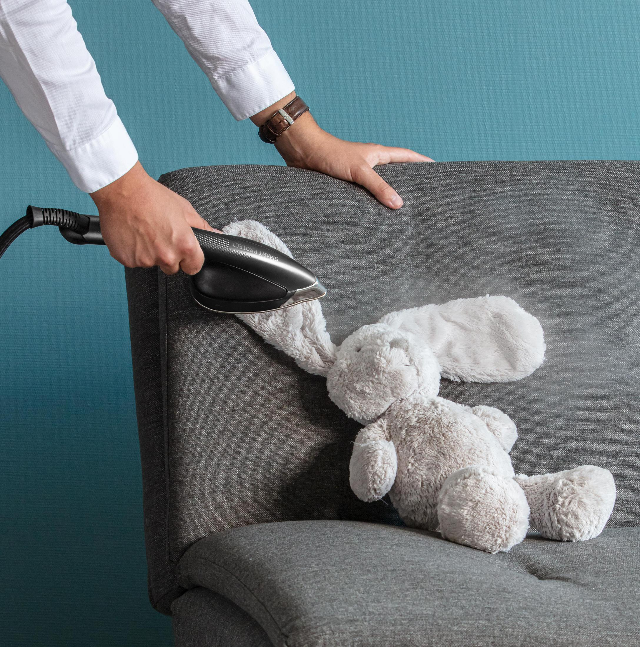 Persona che usa il vapore su un coniglietto di peluche grigio su un divano grigio.