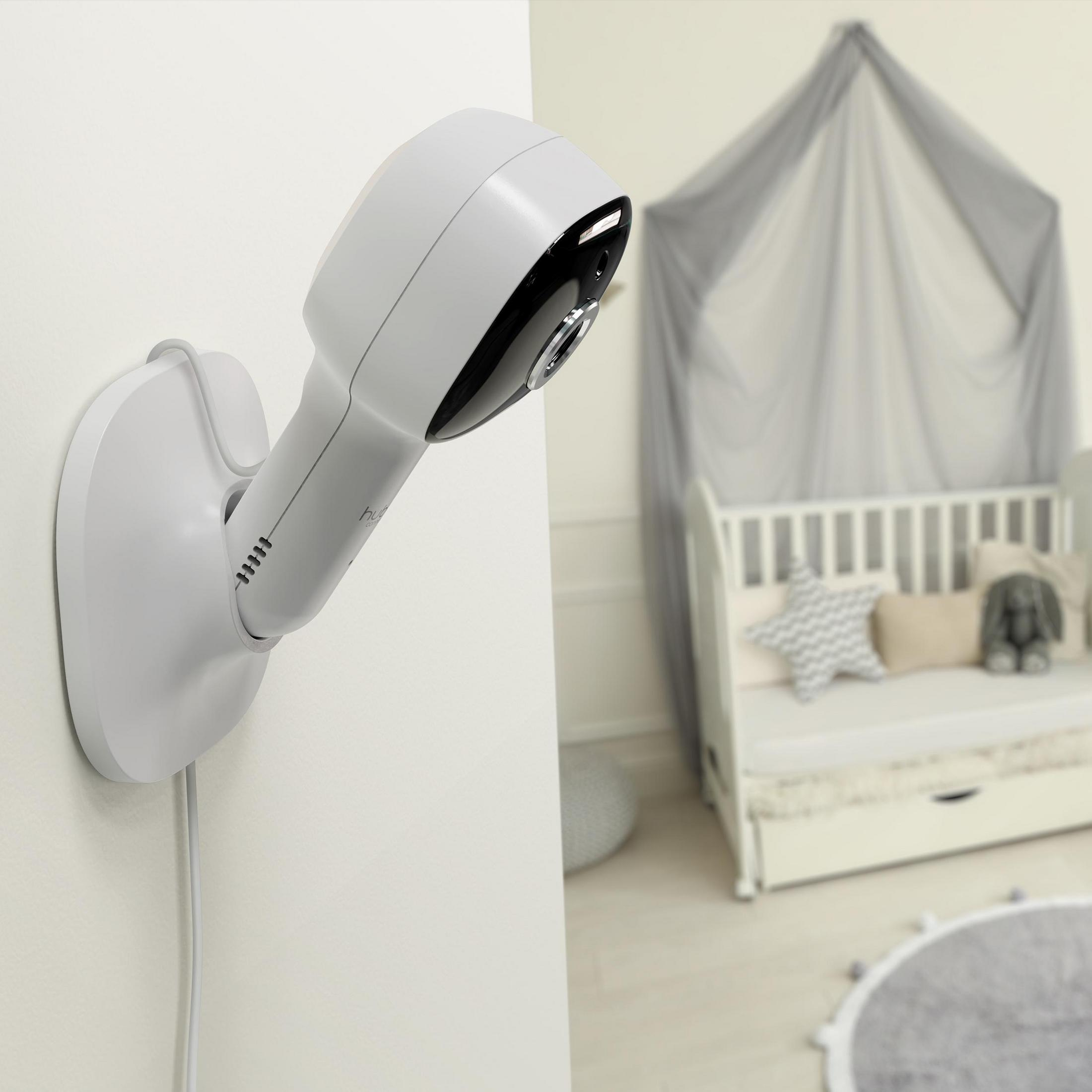 Ein weißer Babyphone an der Wand. Im Hintergrund ist ein Kinderbett zu sehen.