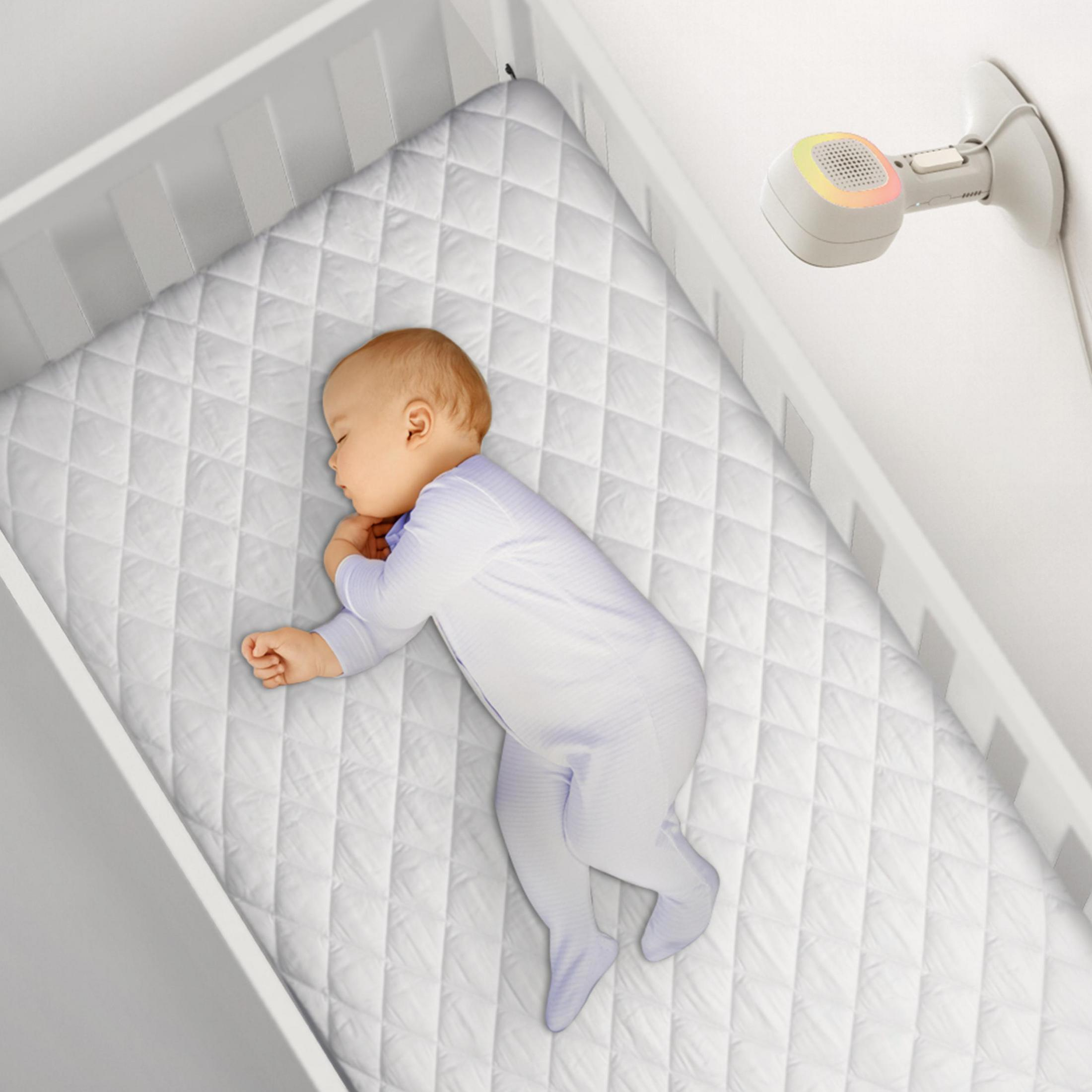 Ein Baby schläft in einem weißen Kinderbett, mit einem weißen und bunten Sensor darüber.