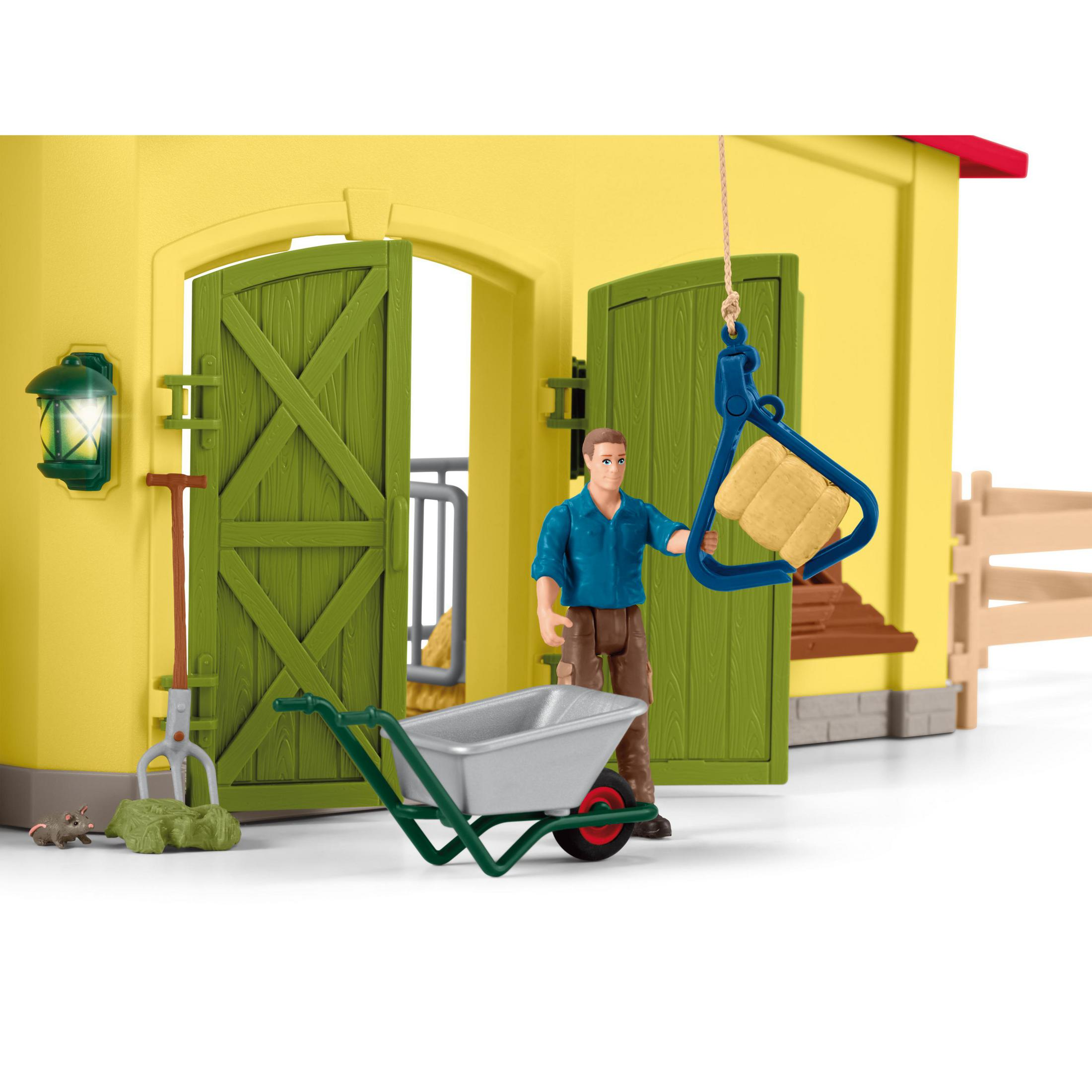 Een speelgoedboerderij met een man, kruiwagen, hooibaal en open schuurdeuren.