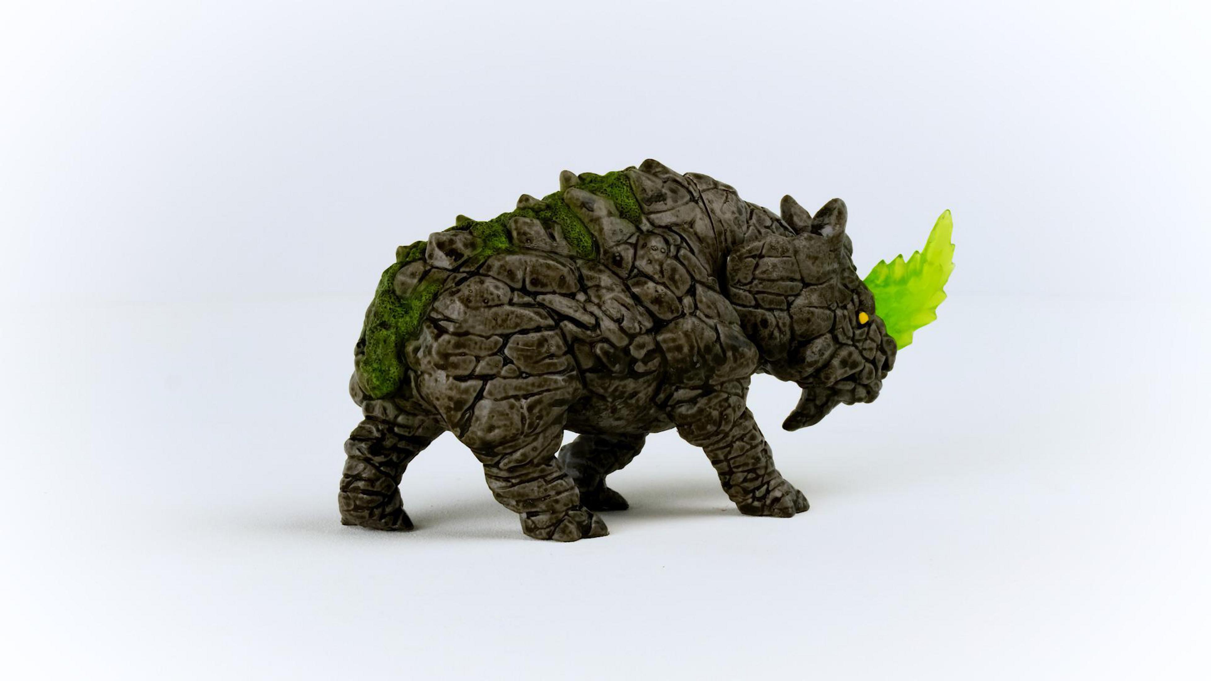 Zabawkowa nosorożec o skalistej fakturze i zielonym mchu. Ma neonowo zielony róg. Białe tło.