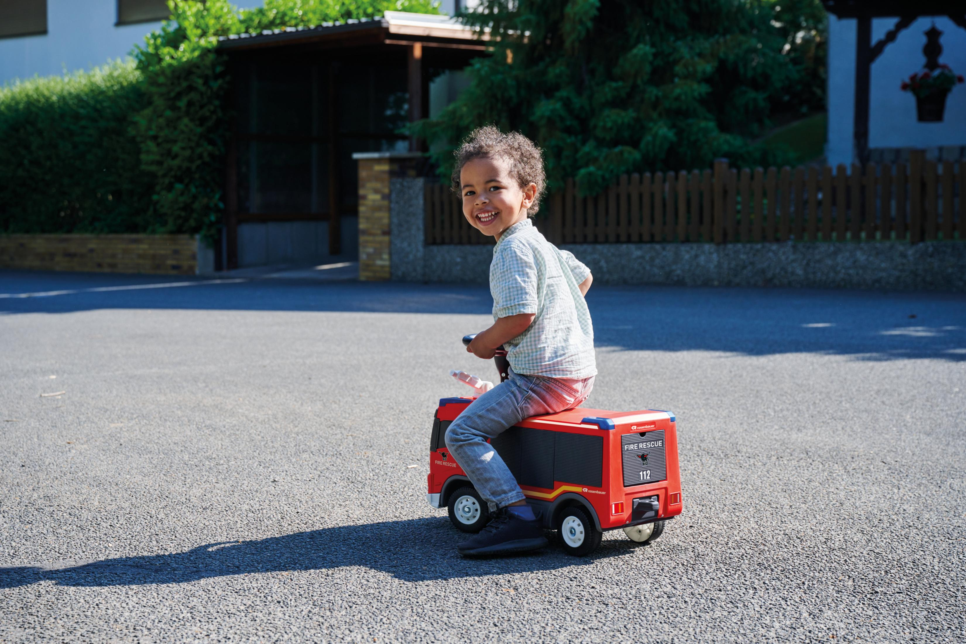 Ein kleiner Junge fährt mit einem Spielzeugfeuerwehrwagen.