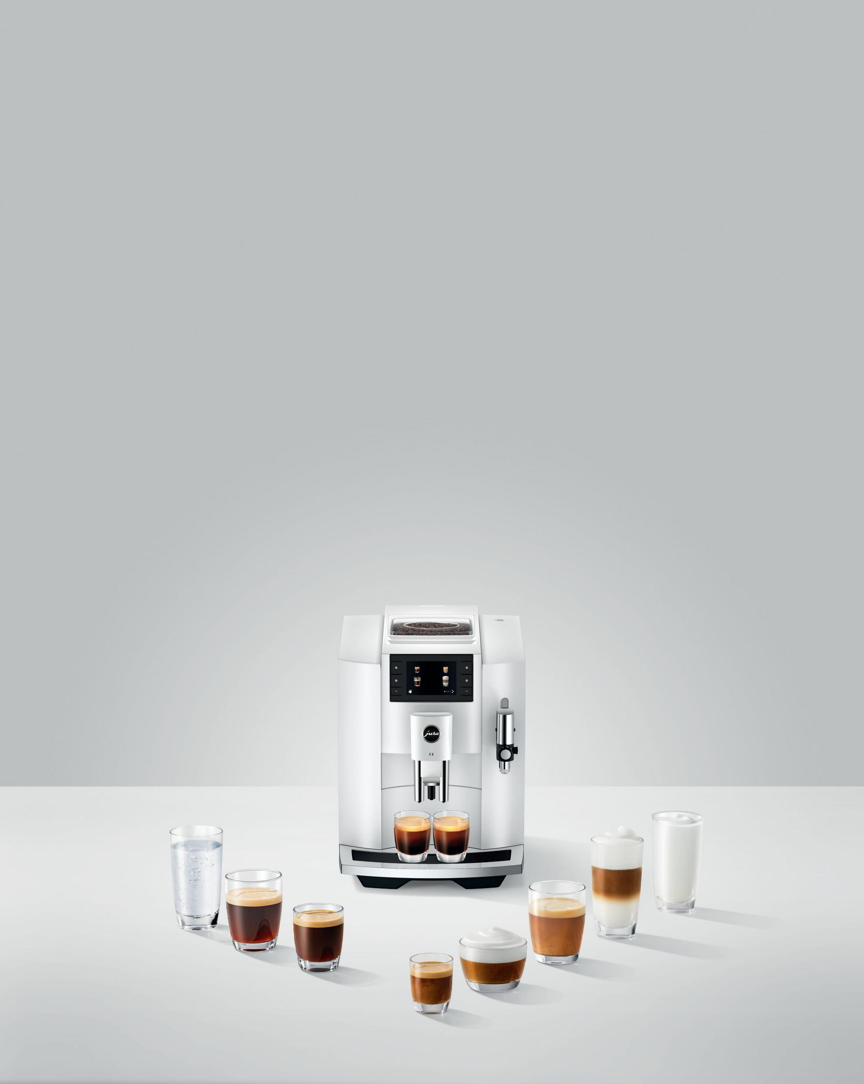 Weiße Kaffeemaschine mit verschiedenen Kaffeegetränken in Gläsern.