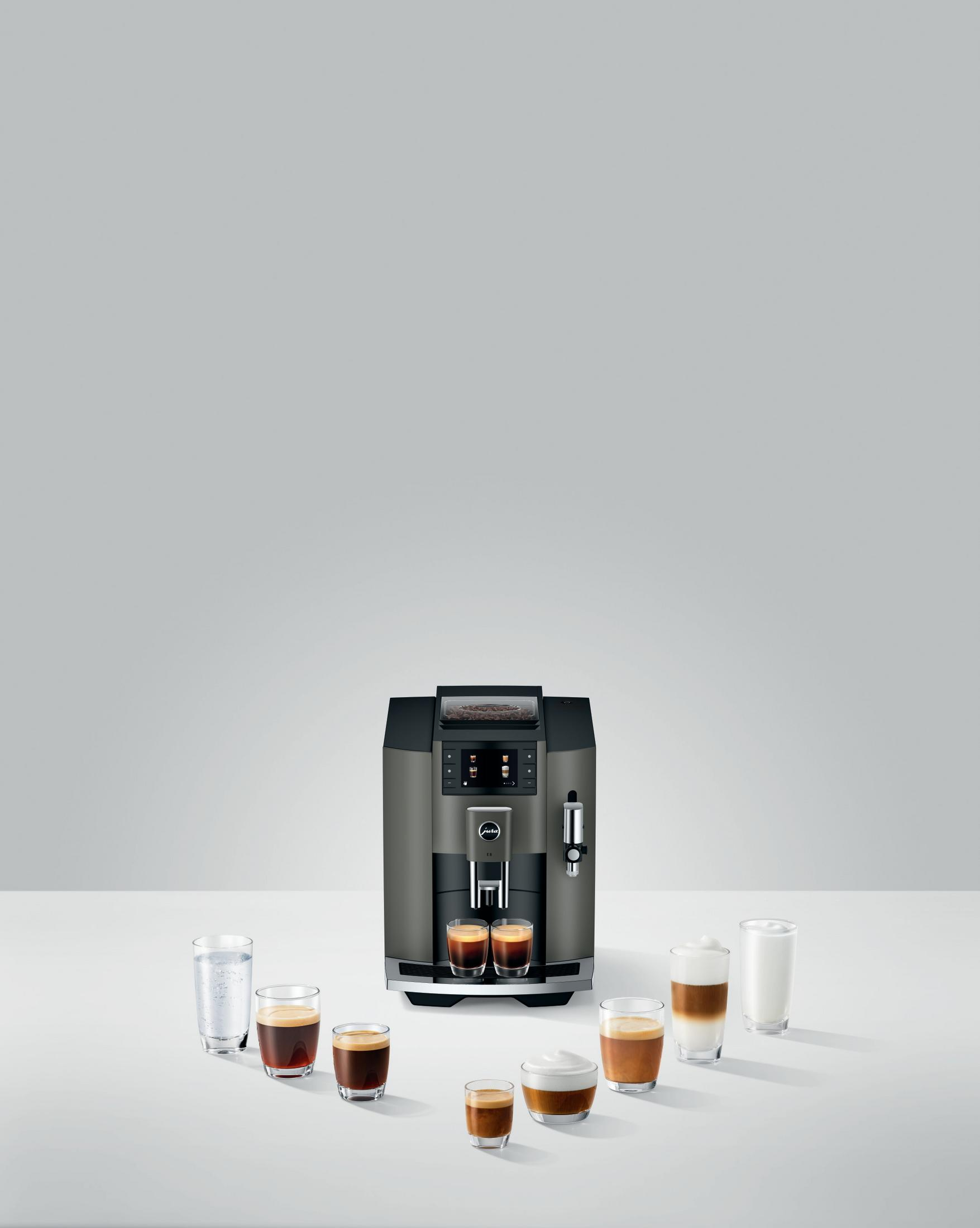 Eine graue Kaffeemaschine mit verschiedenen Kaffeegläsern, die um sie herum angeordnet sind. Die Maschine steht auf einer weißen Oberfläche.