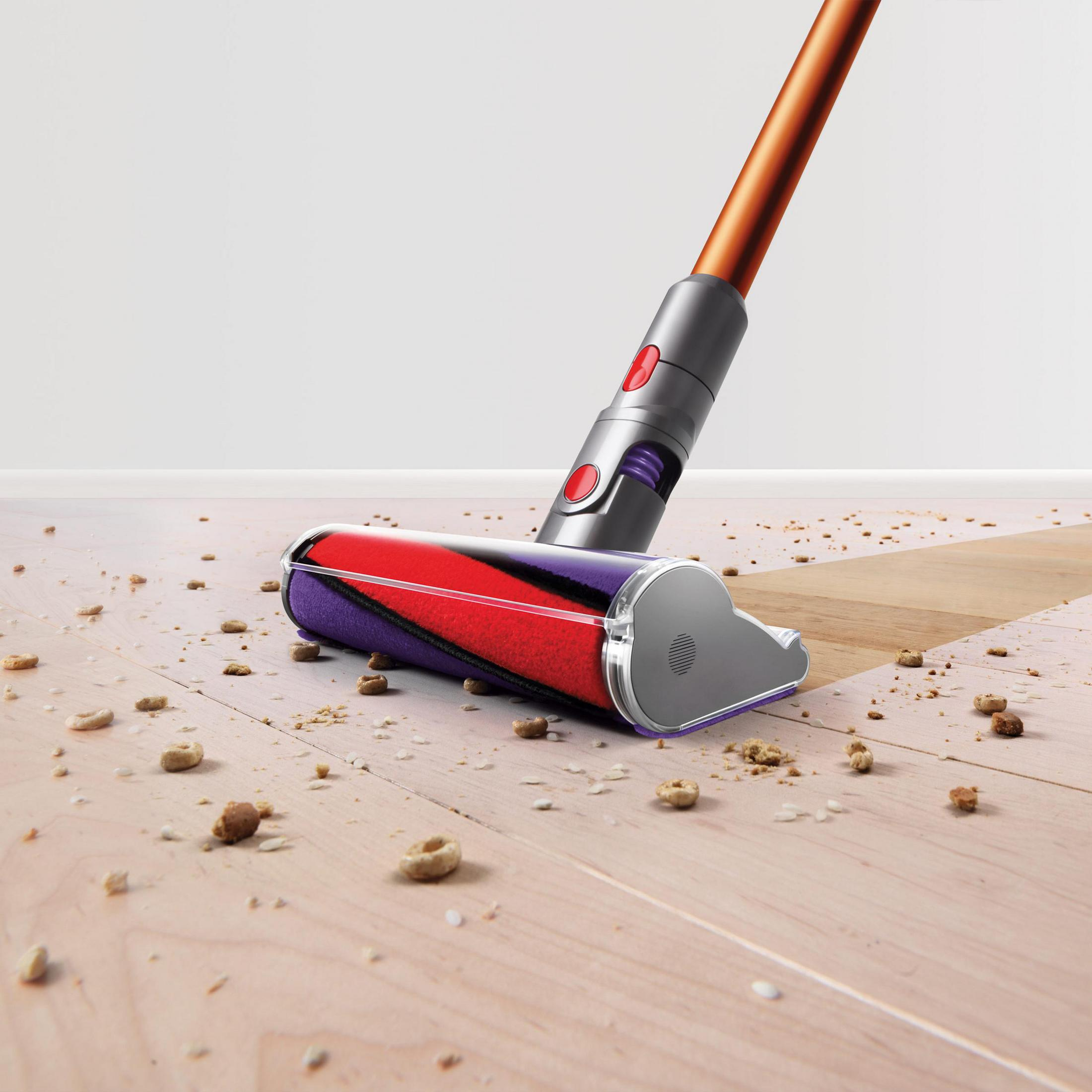 Głowica odkurzacza na drewnianej podłodze, zbierająca okruchy. Widoczny jest czerwono-fioletowy wałek.