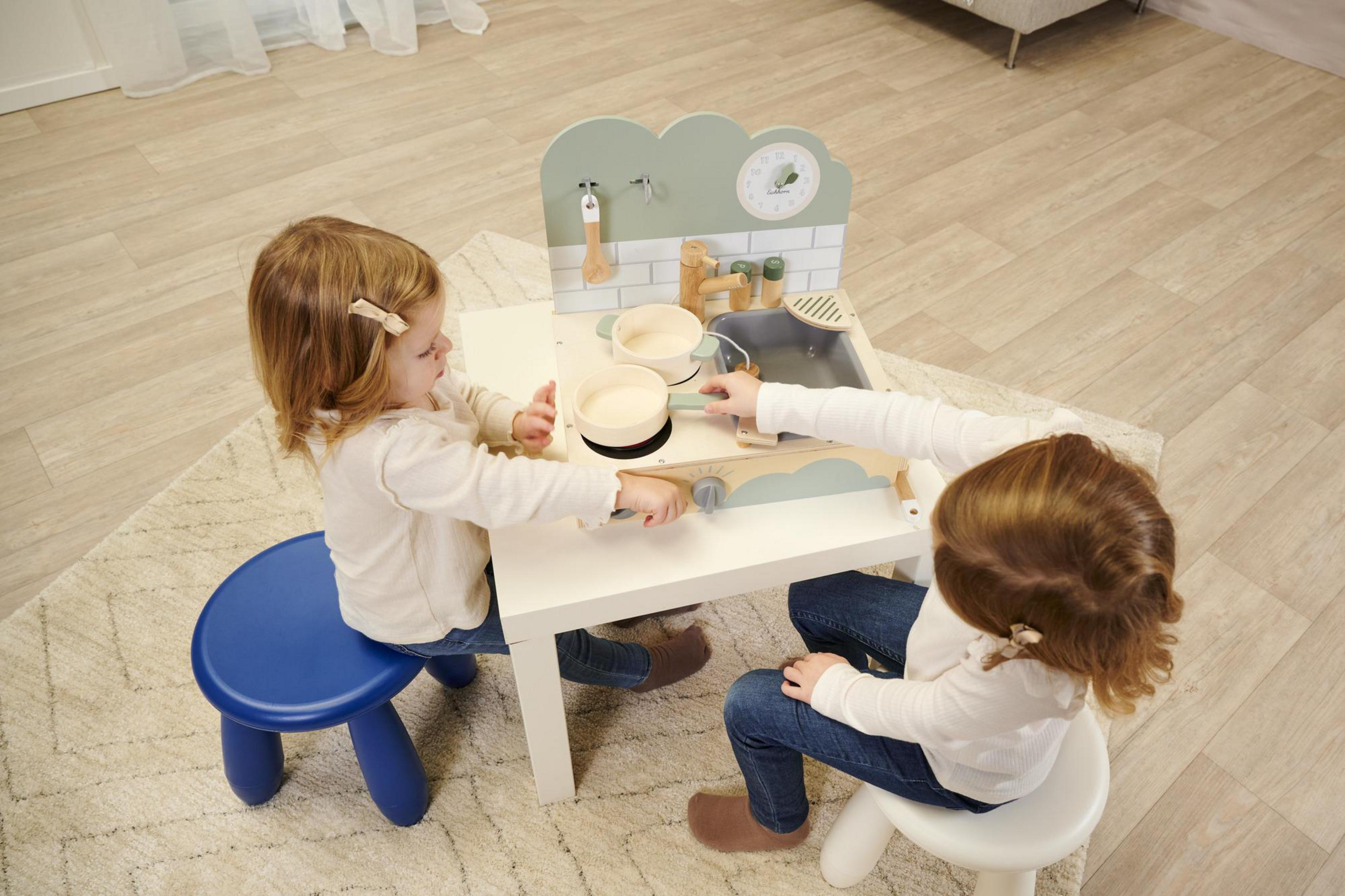 Zwei Mädchen spielen mit einer Spielzeugküche. Weißer Hintergrund.