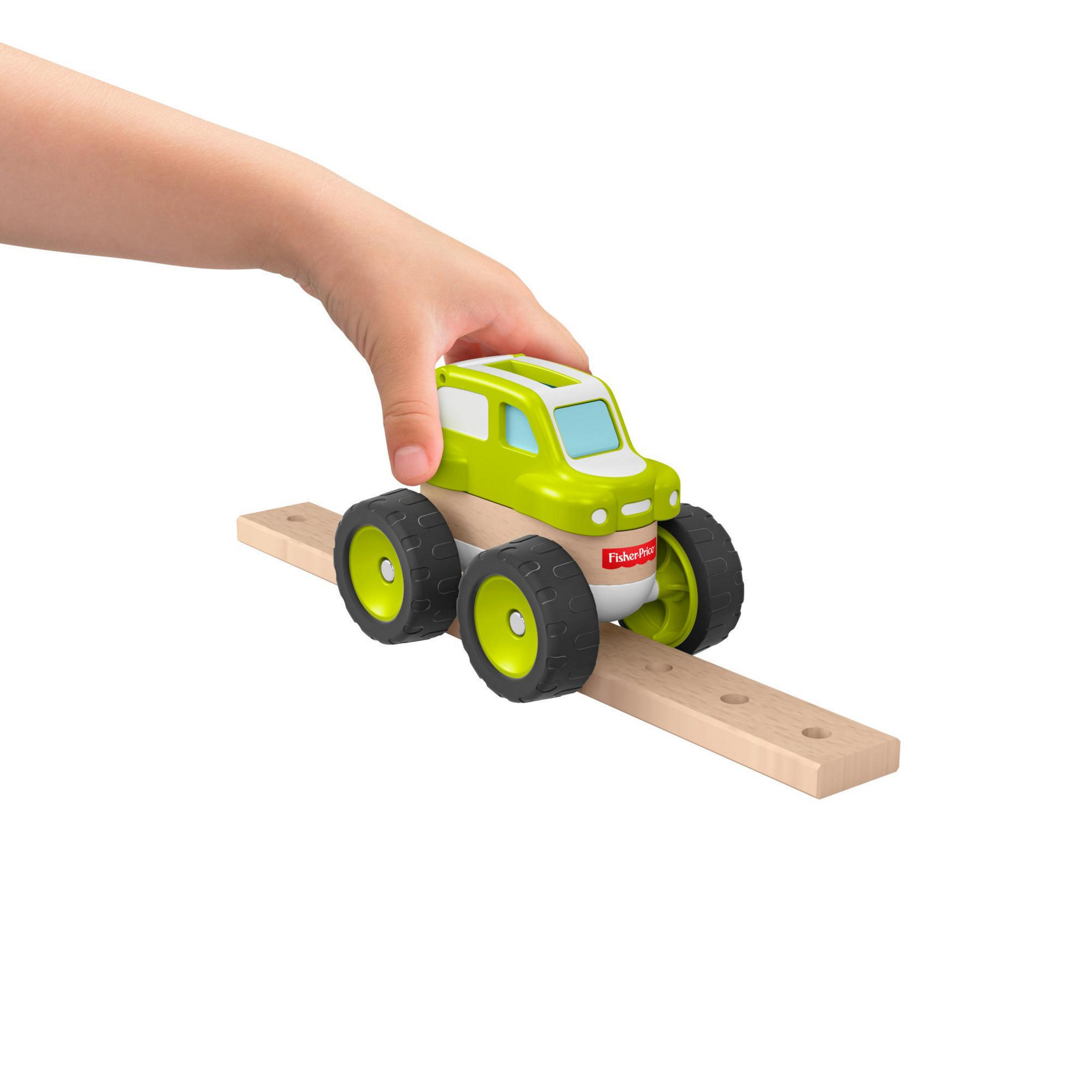 Die Hand eines Kindes schiebt ein grün-weißes Spielzeugauto mit großen schwarzen Rädern auf einer Holzstrecke.