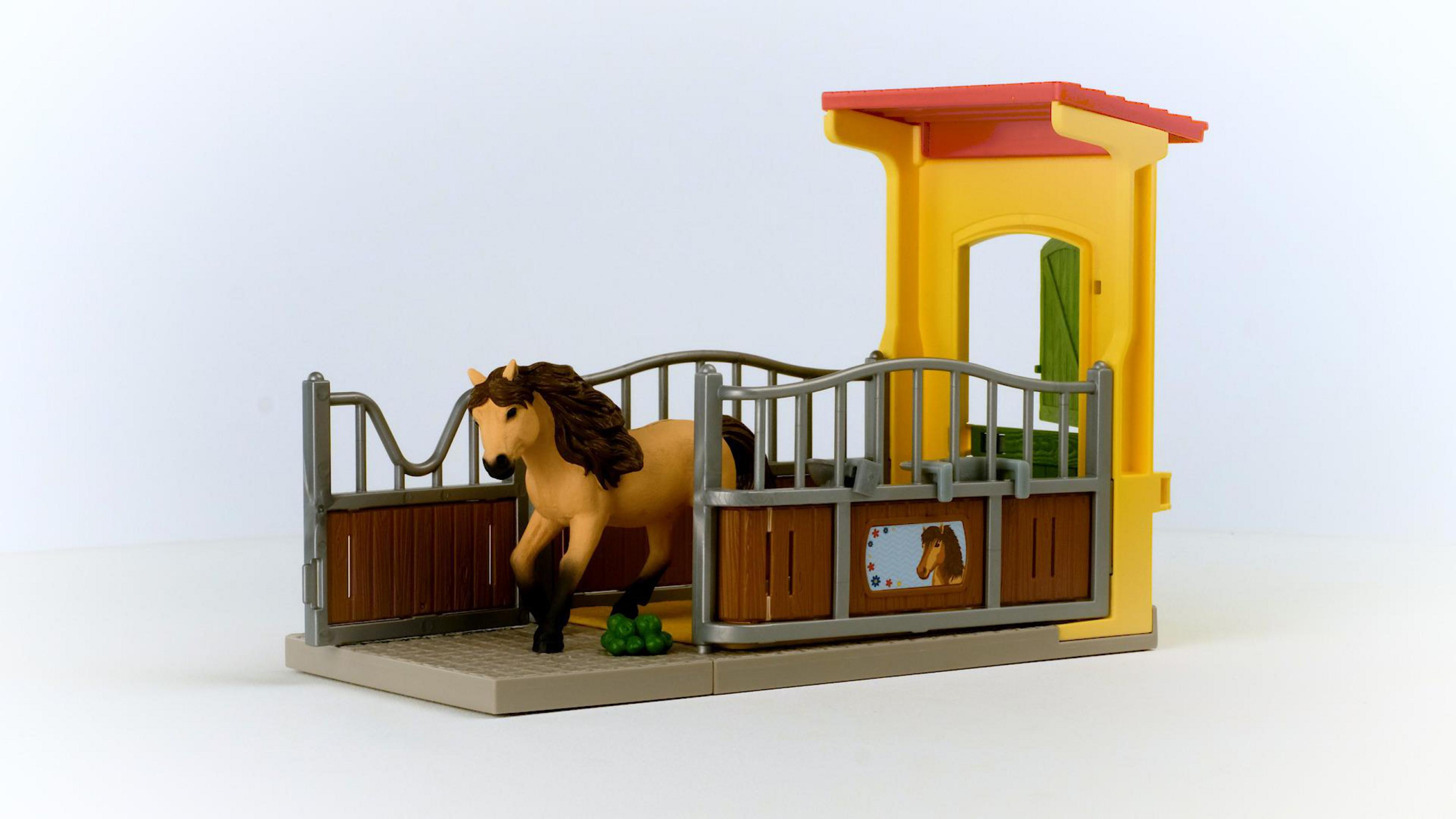 Ein Spielzeugpferd in einem Stall. Das Pferd ist braun und hellbraun; der Stall ist gelb und braun.