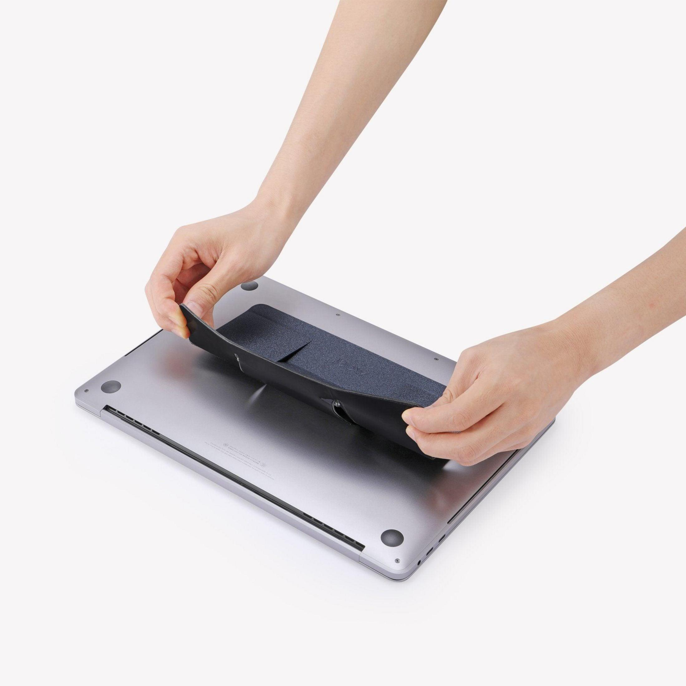 Hände befestigen eine schwarze Laptop-Hülle an einem silbernen Laptop, vor weißem Hintergrund.