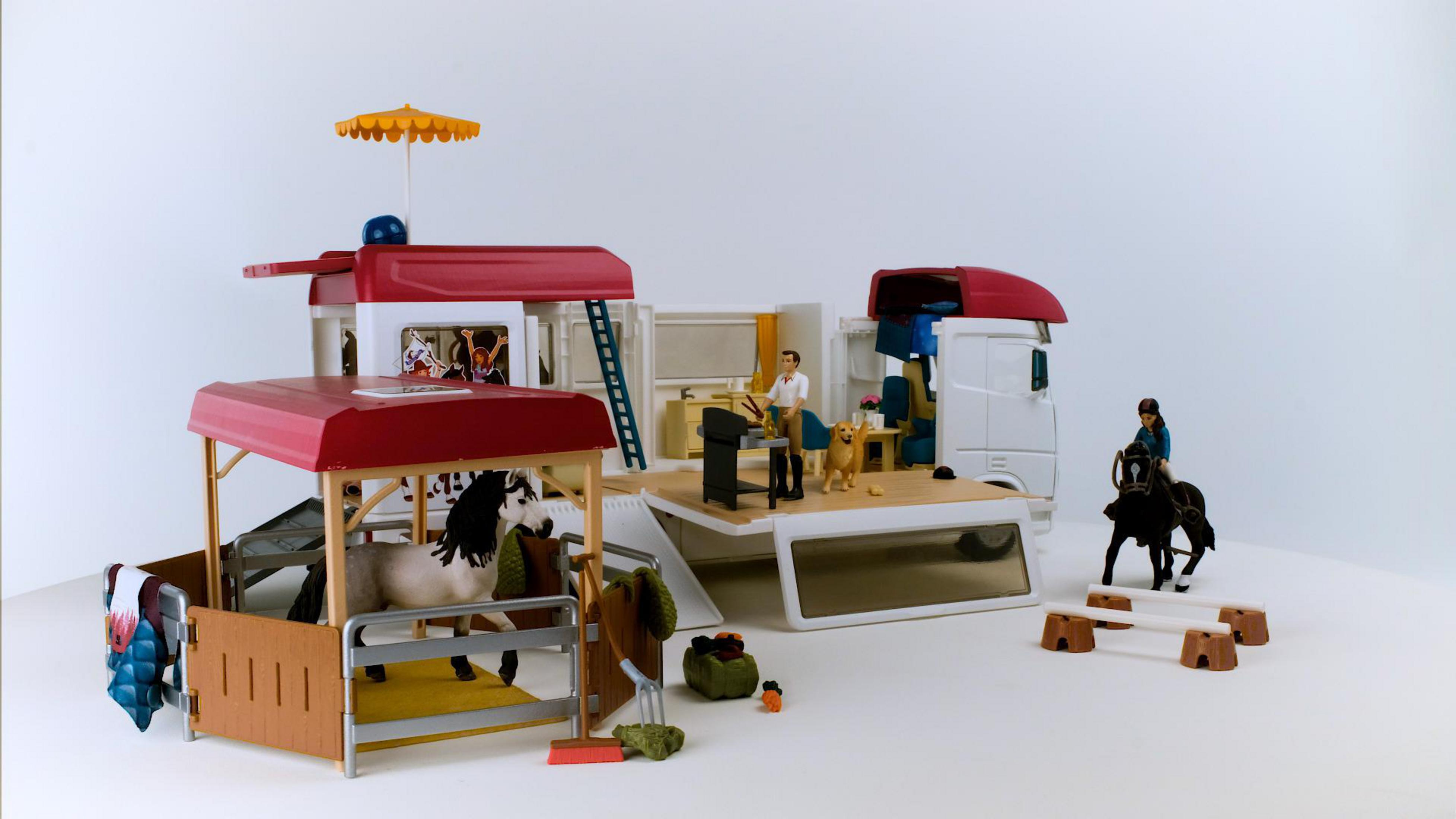 Zabawkowa stajnia z ciężarówką, końmi, ludźmi i akcesoriami na białej powierzchni.