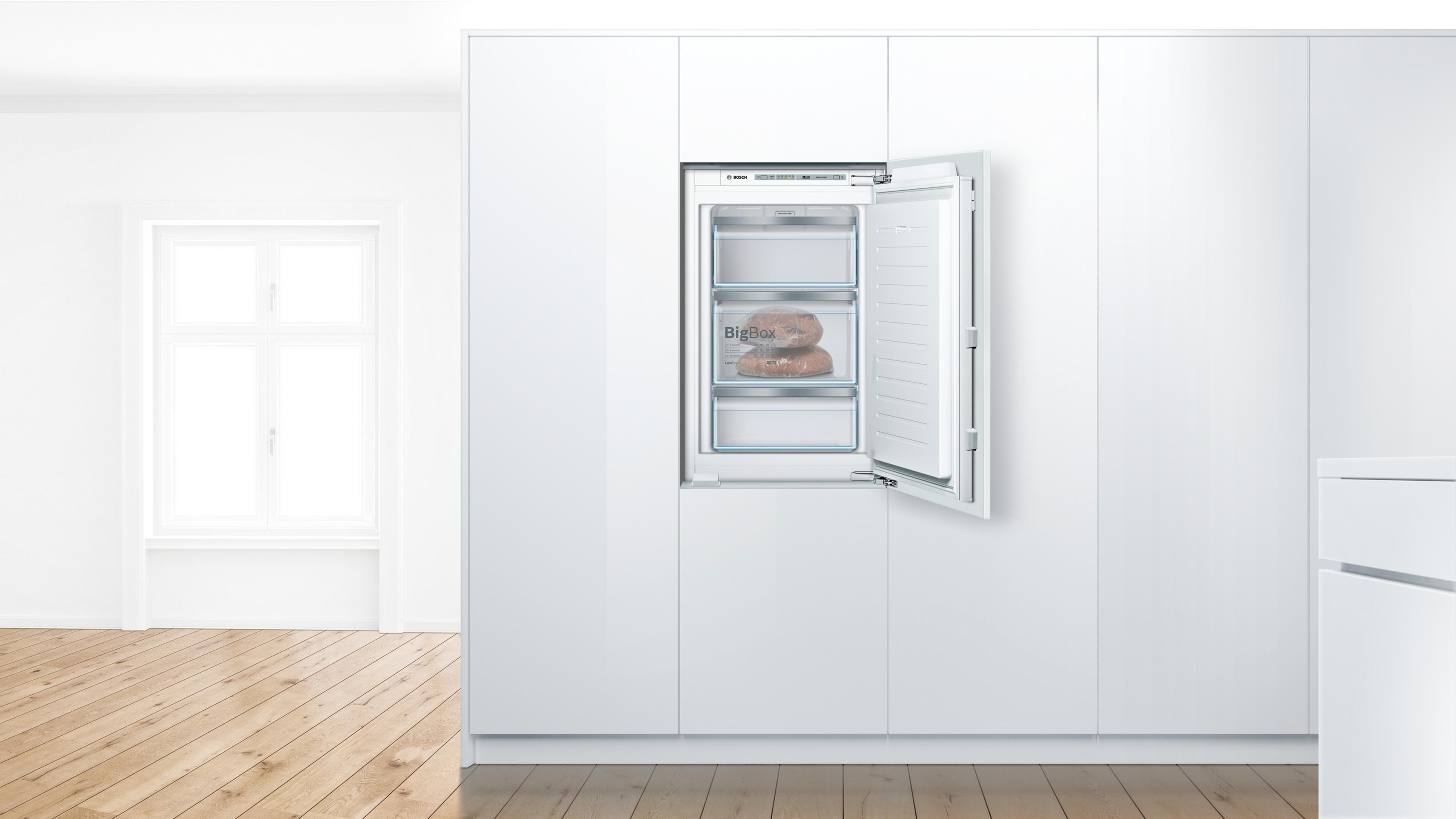 Frigorifero bianco a incasso con tre cassetti aperti, all'interno di un mobile bianco, in una stanza bianca.