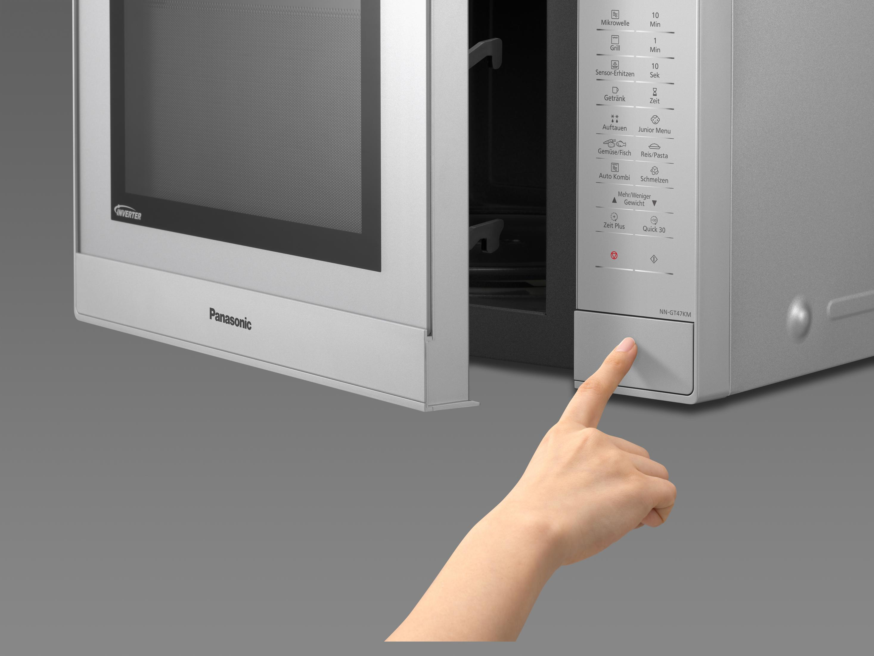 Palec naciska przycisk na kuchence mikrofalowej Panasonic. Szare tło.