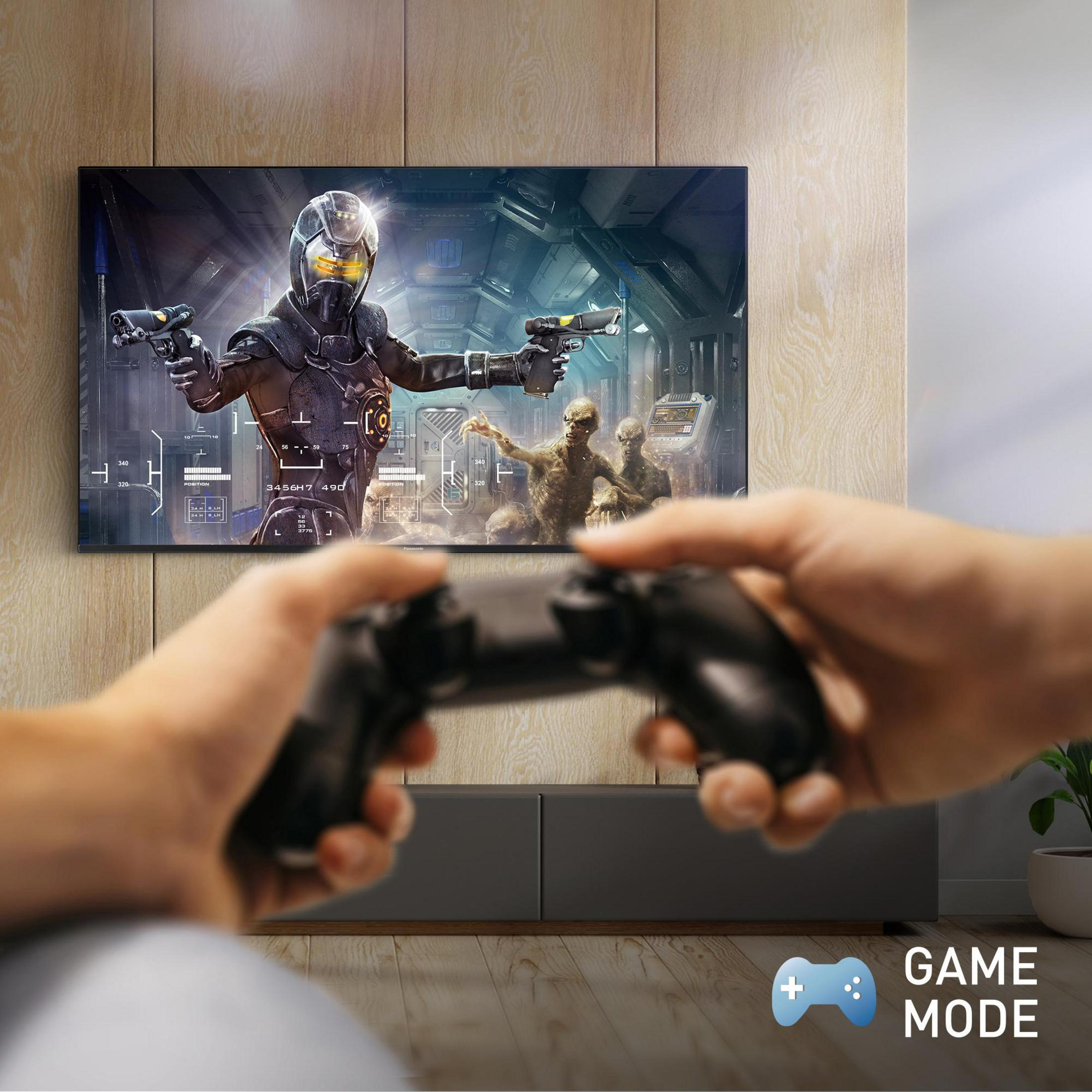 Persona che tiene in mano un controller davanti a uno schermo TV con grafica di gioco. Testo Modalità Gioco.