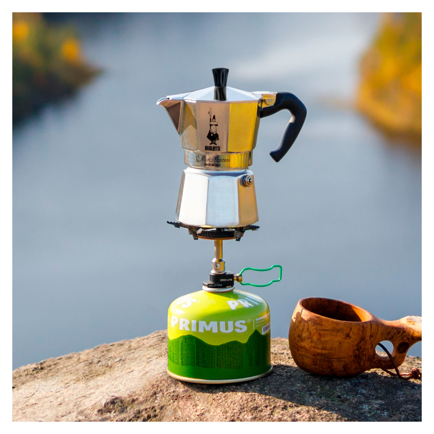 Kawiarka na kuchence gazowej z zieloną butlą gazową i drewnianym kubkiem, na zewnątrz.