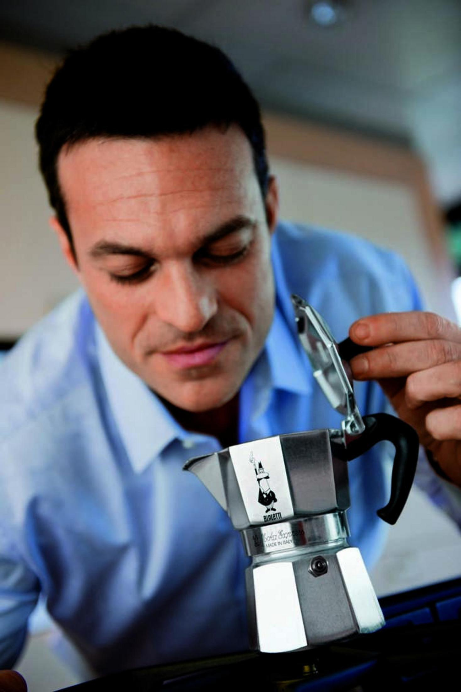 Mężczyzna zagląda do srebrnego ekspresu do kawy, otwierając go prawą ręką. Zbliżenie na maszynę.