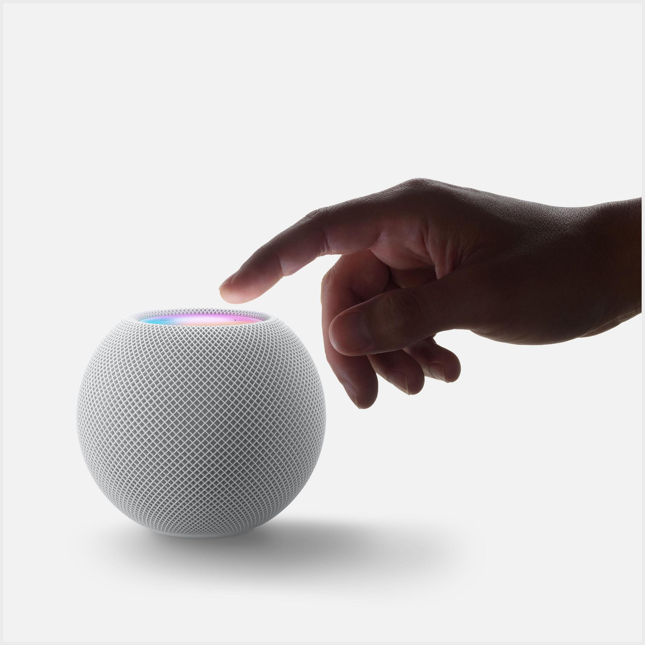 Dłoń dotykająca białego Apple HomePod, z tęczowym światłem, na białym tle.