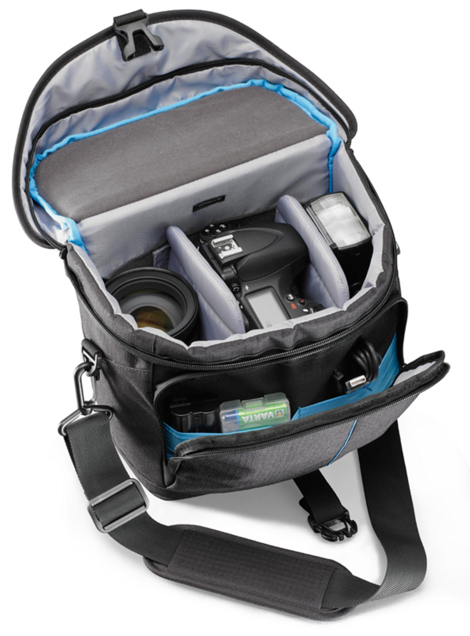 Offene Kameratasche mit Kamera, Objektiv, Blitz und Zubehör. Innenraum ist grau mit blauen Akzenten und Taschen.
