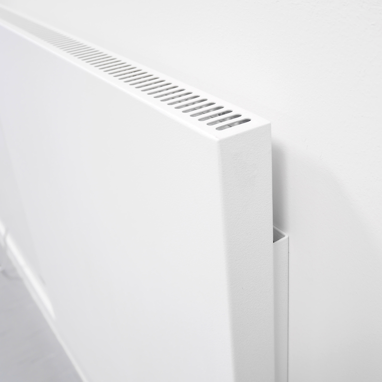 Ein weißer elektrischer Heizkörper, der an einer weißen Wand montiert ist, Seitenansicht.