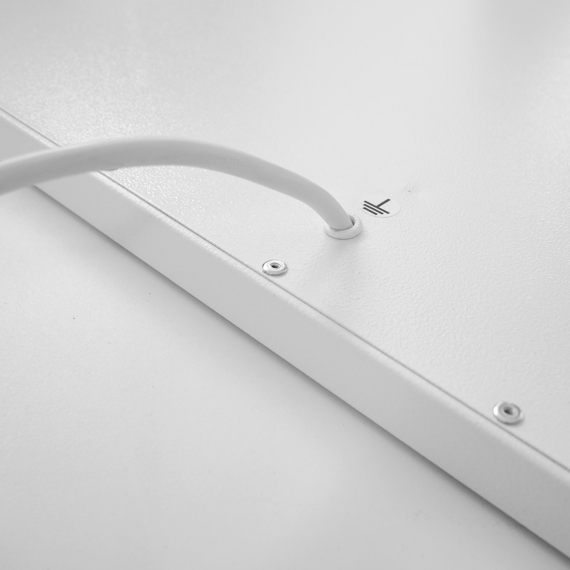Nahaufnahme einer weißen Platte mit einem Kabel, das durch ein Loch gesteckt wird, Schrauben sichtbar.