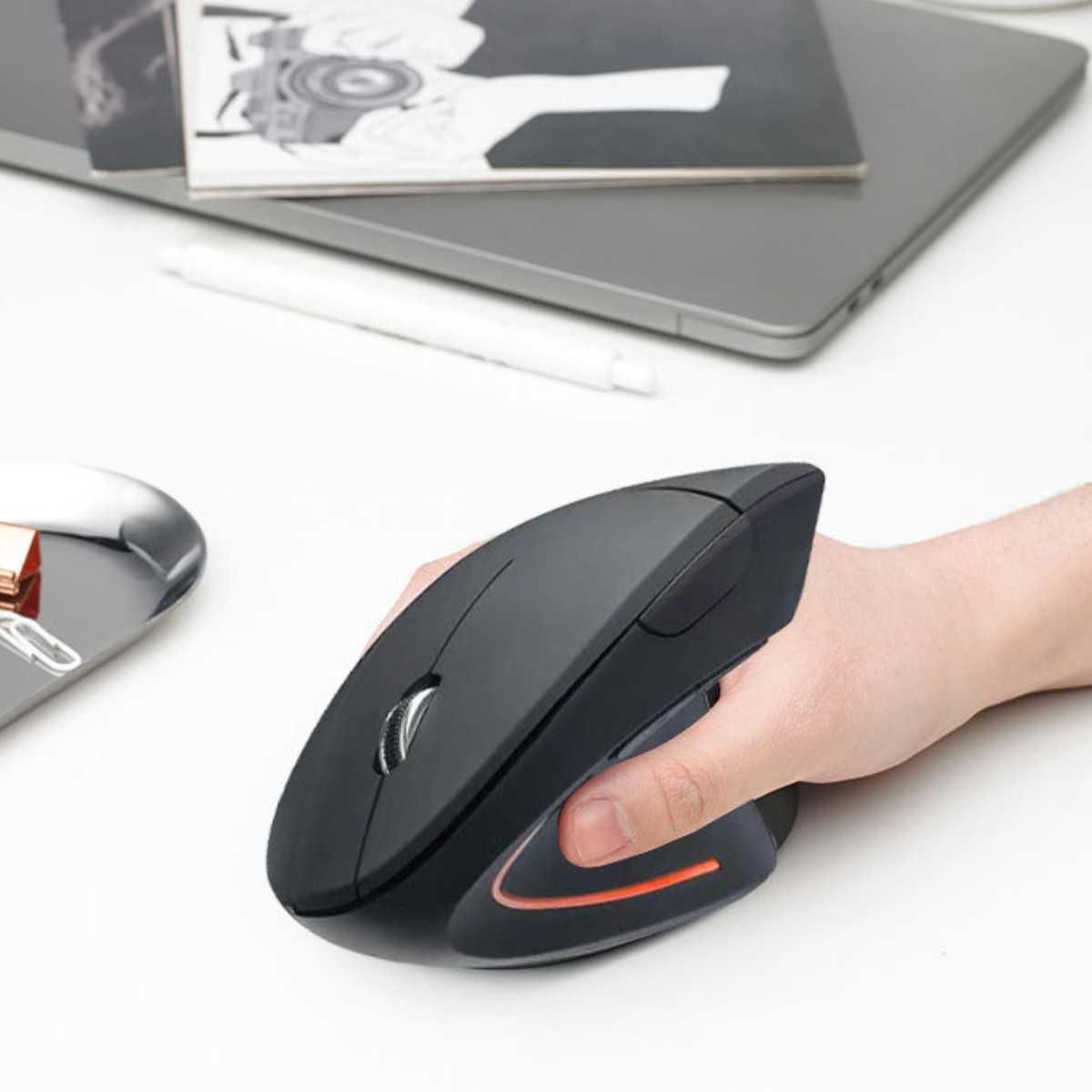 Hand, die eine schwarze ergonomische Maus hält. Weiße Oberfläche, grauer Laptop.