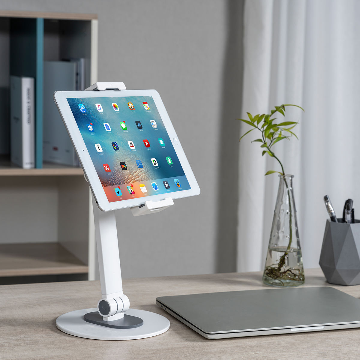 Tablette blanche sur un support sur un bureau, avec un ordinateur portable et une plante.