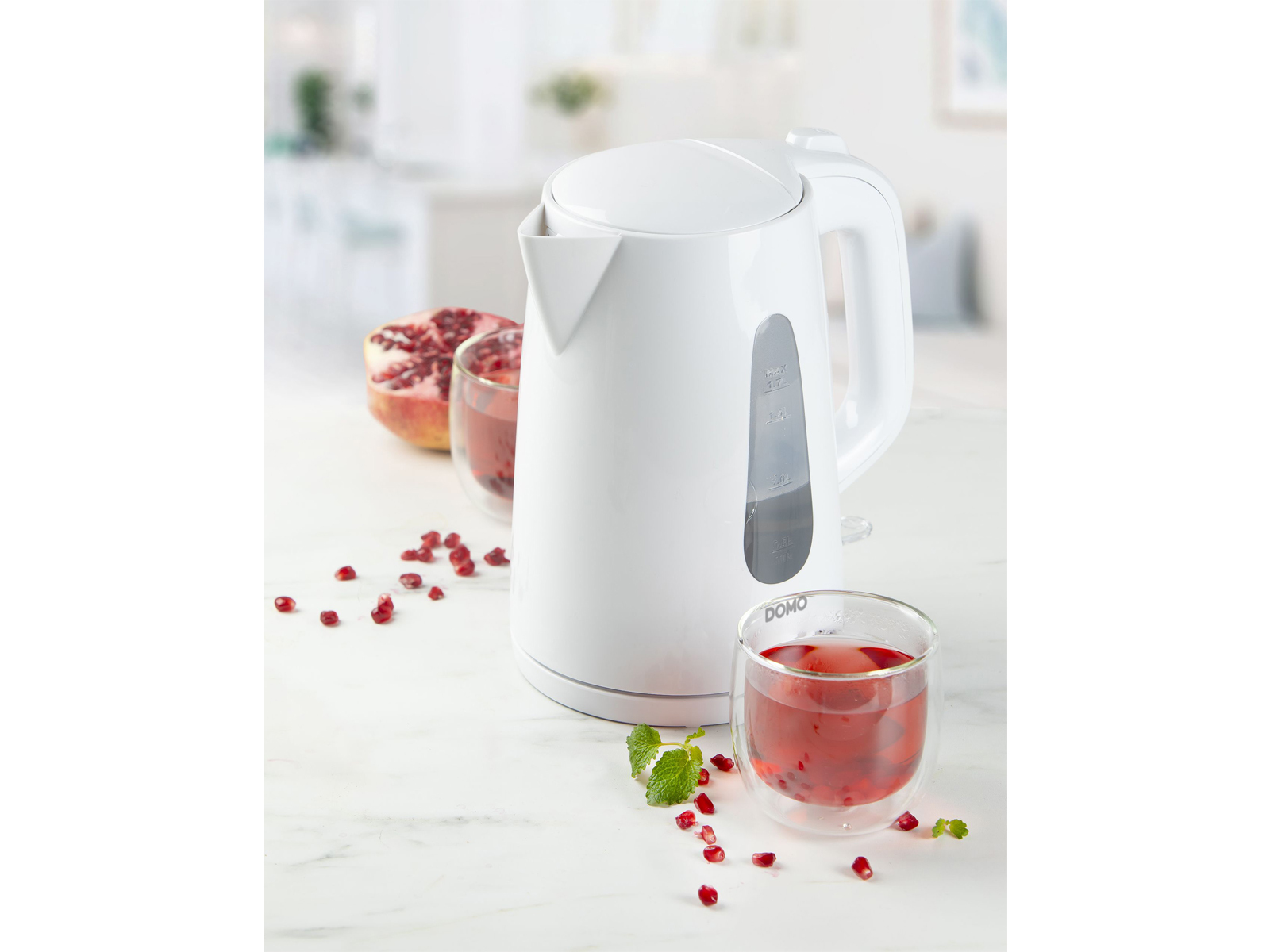 Bollitore elettrico bianco, melograno e bicchieri con liquido rosso.