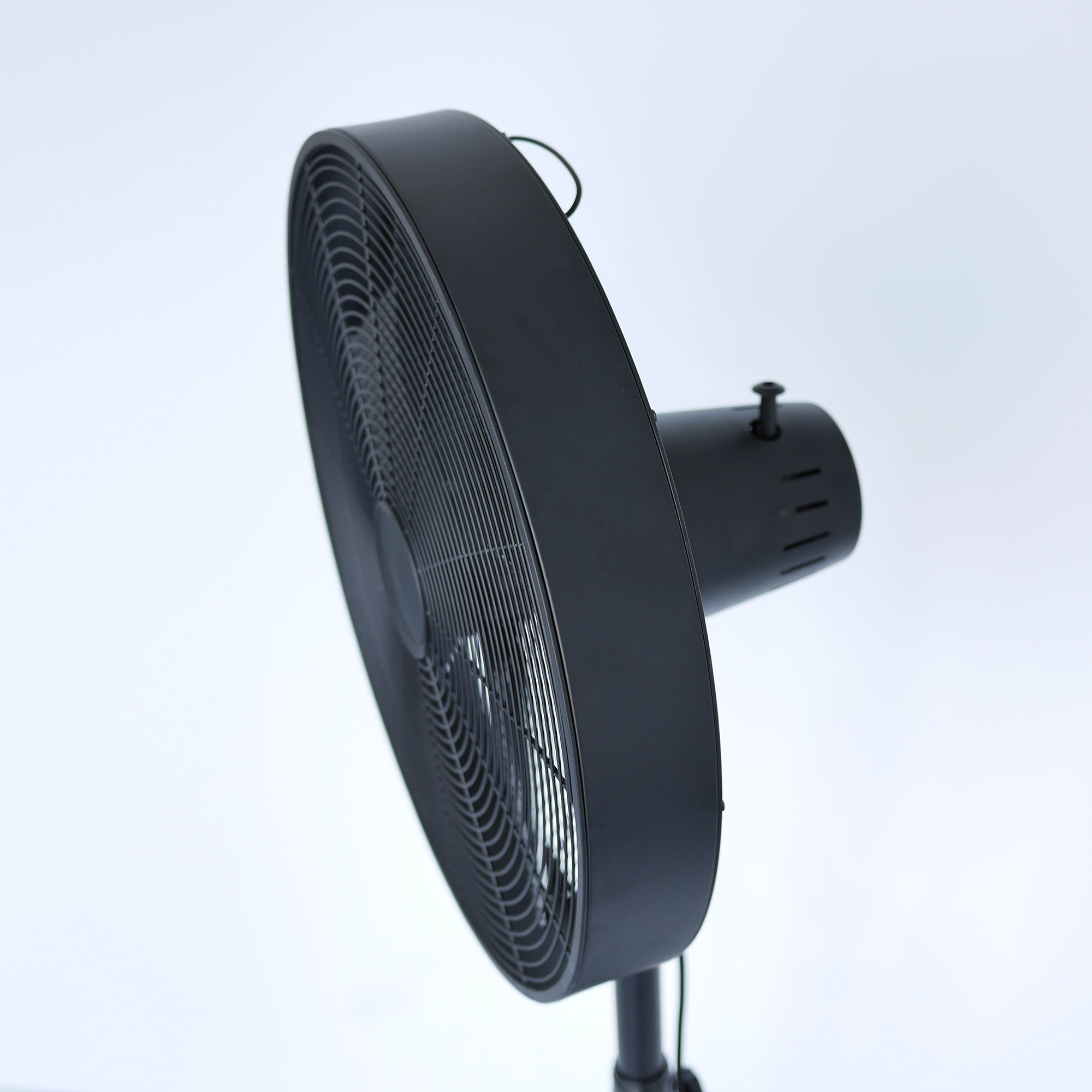 Schwarzer elektrischer Ventilator, schräg vor weißem Hintergrund positioniert, Seitenansicht.