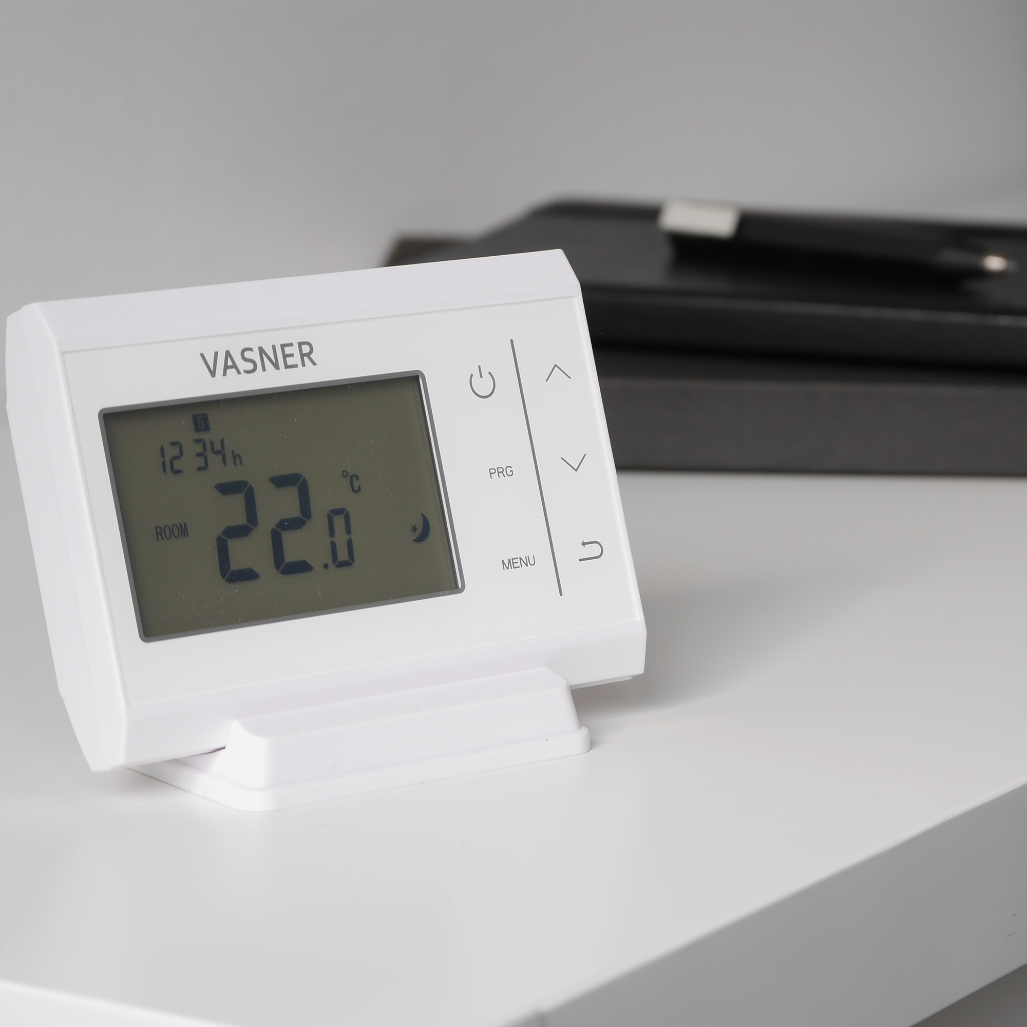 Ein weißes Smart-Thermostat zeigt die Raumtemperatur, Uhrzeit und Steuertasten auf weißer Oberfläche an.