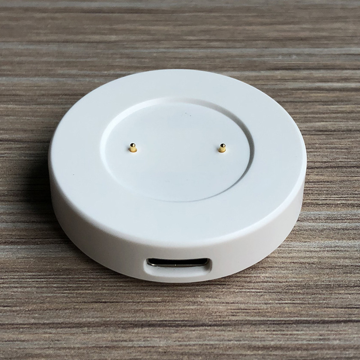 Biała okrągła podstawa do ładowania zegarka z dwoma złotymi pinami i portem USB.