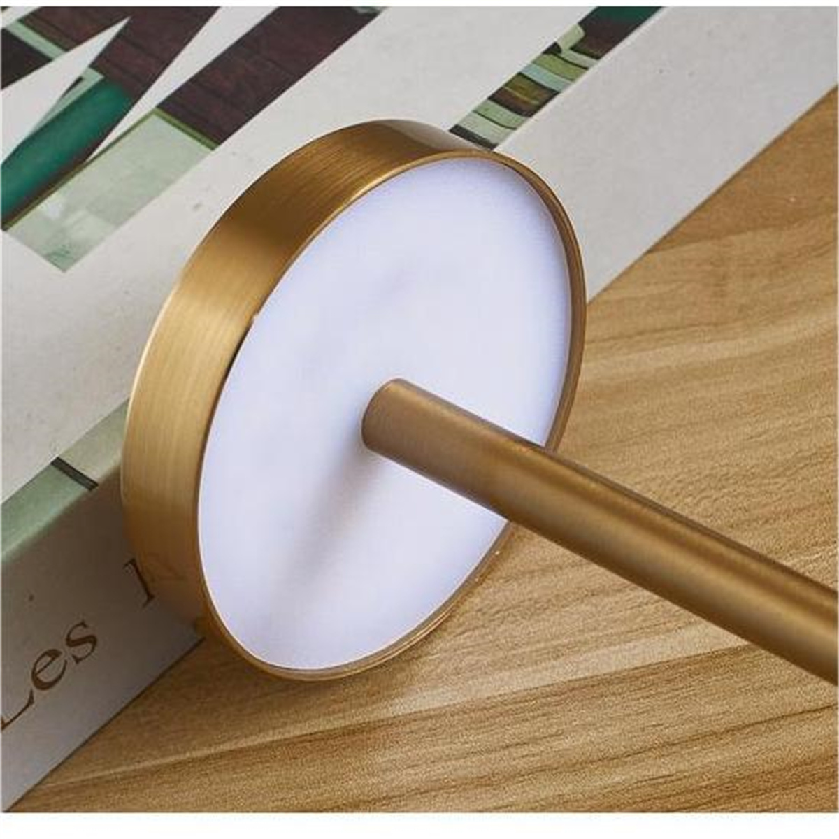 Eine weiße, scheibenförmige Lampe mit goldfarbenem Stiel, die auf einem Buch liegt.
