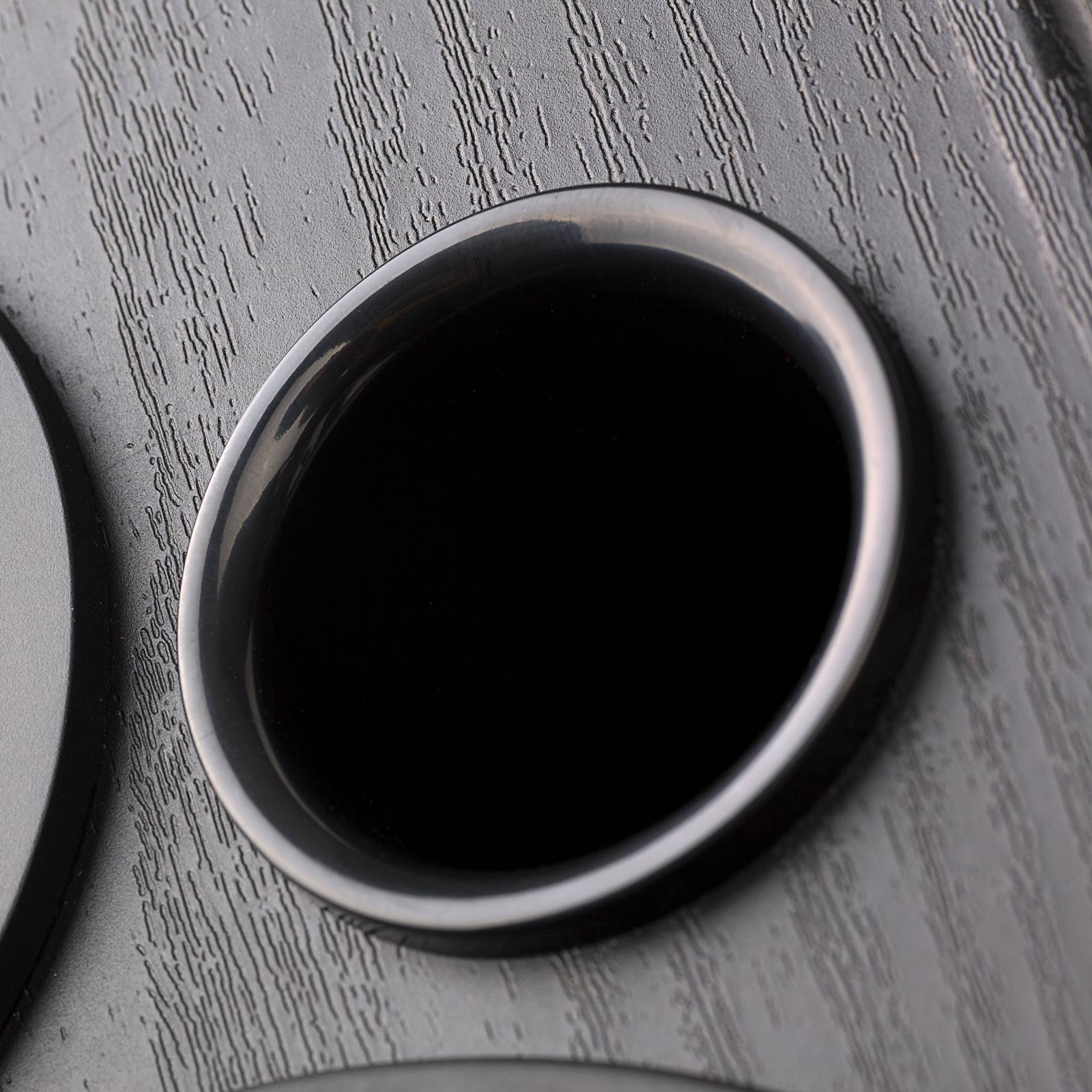 Zbliżenie czarnego otworu wentylacyjnego głośnika z błyszczącym, owalnym otworem.