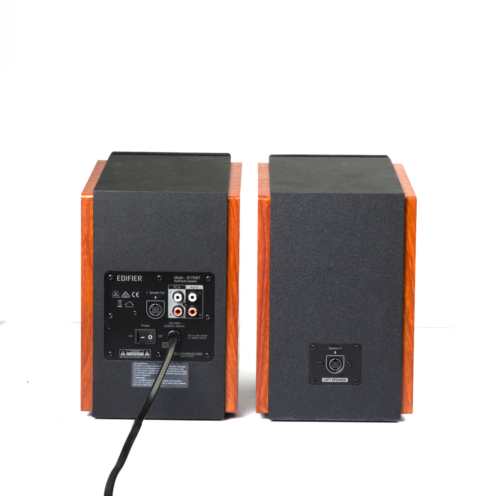 Dwa drewniane głośniki na białym tle. Czarne tyły z przyciskami i portami. Pomarańczowo-brązowe boki.