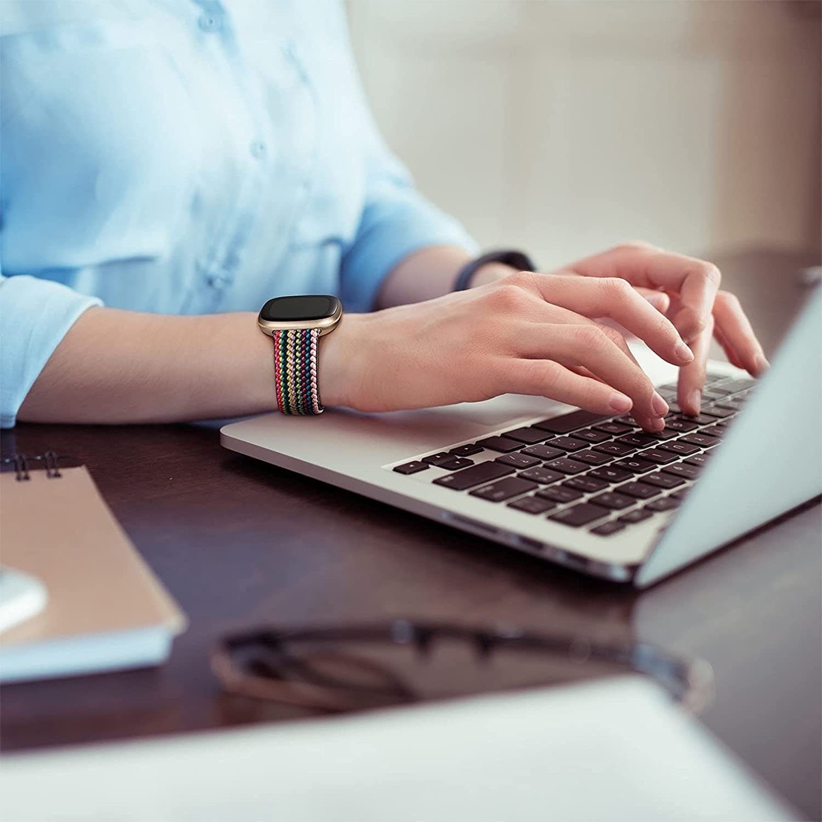 Eine Frau tippt auf einem Laptop, bunte Armbanduhr am Handgelenk.