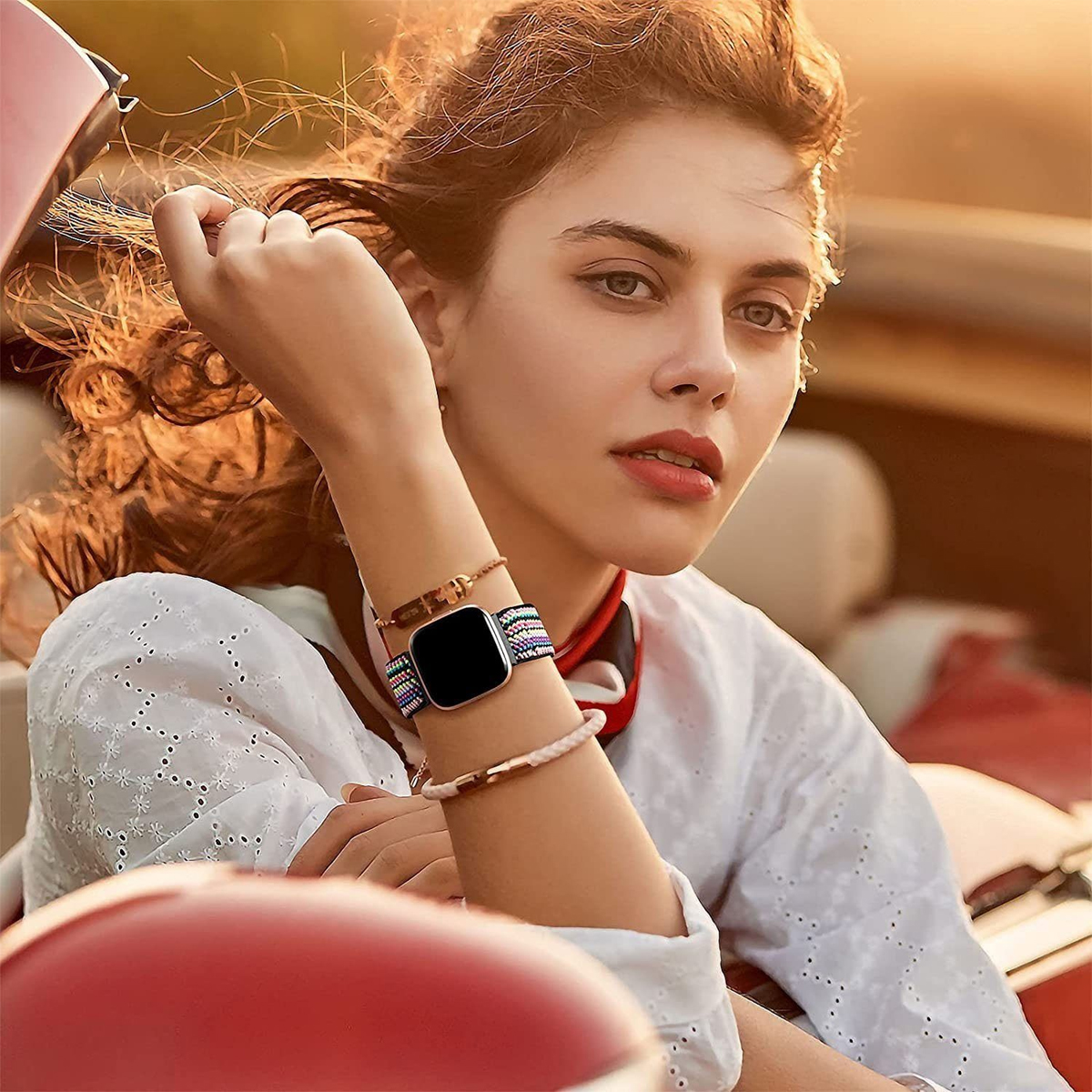 Eine Frau trägt eine Smartwatch, Armbänder und ein weißes Hemd, mit einem Auto im Hintergrund.