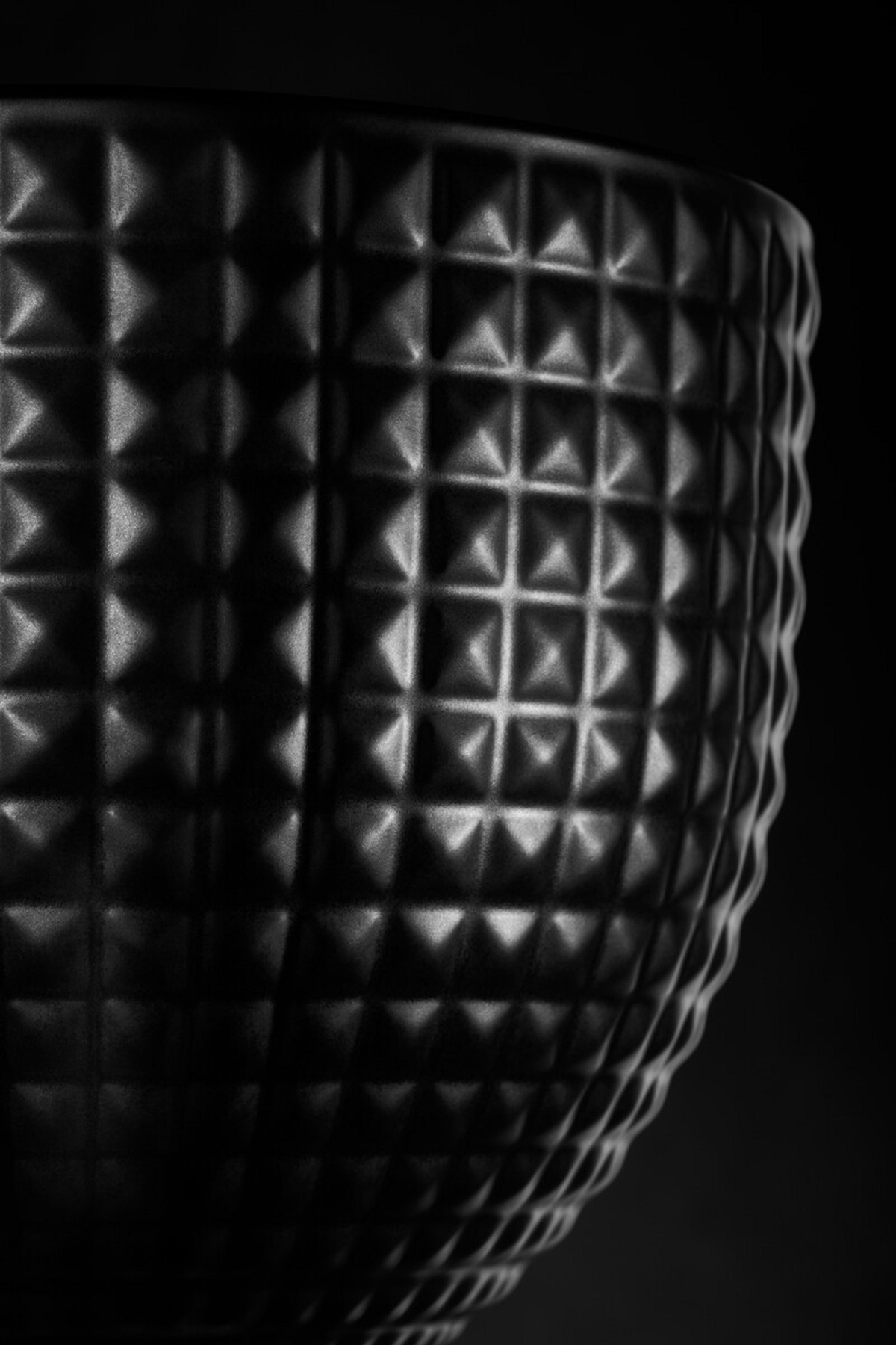 Nahaufnahme einer schwarzen, strukturierten Vase mit geometrischem Muster, vor dunklem Hintergrund.