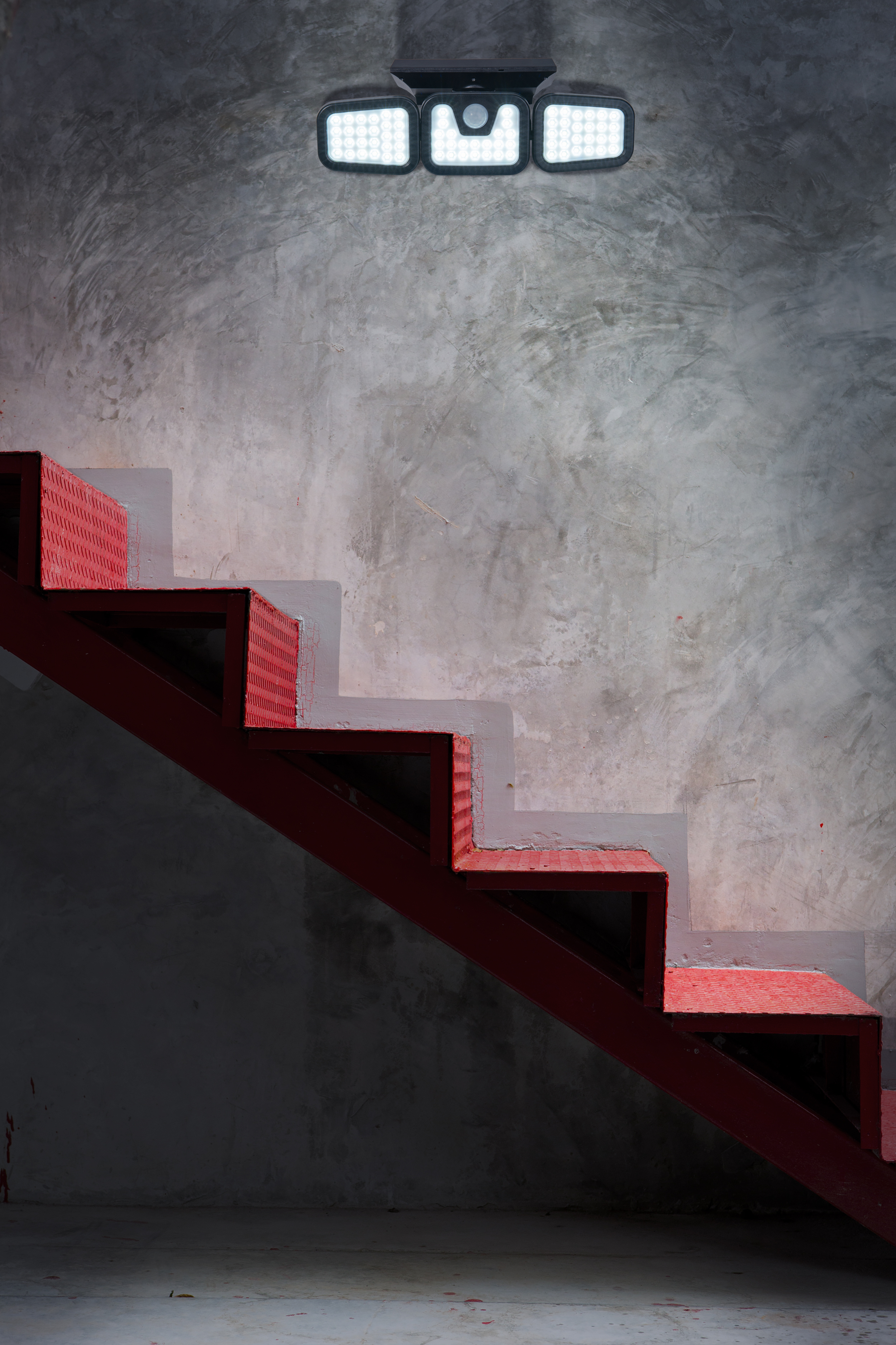 Rote Metalltreppe mit Licht, an einer grau strukturierten Wand befestigt, absteigend.